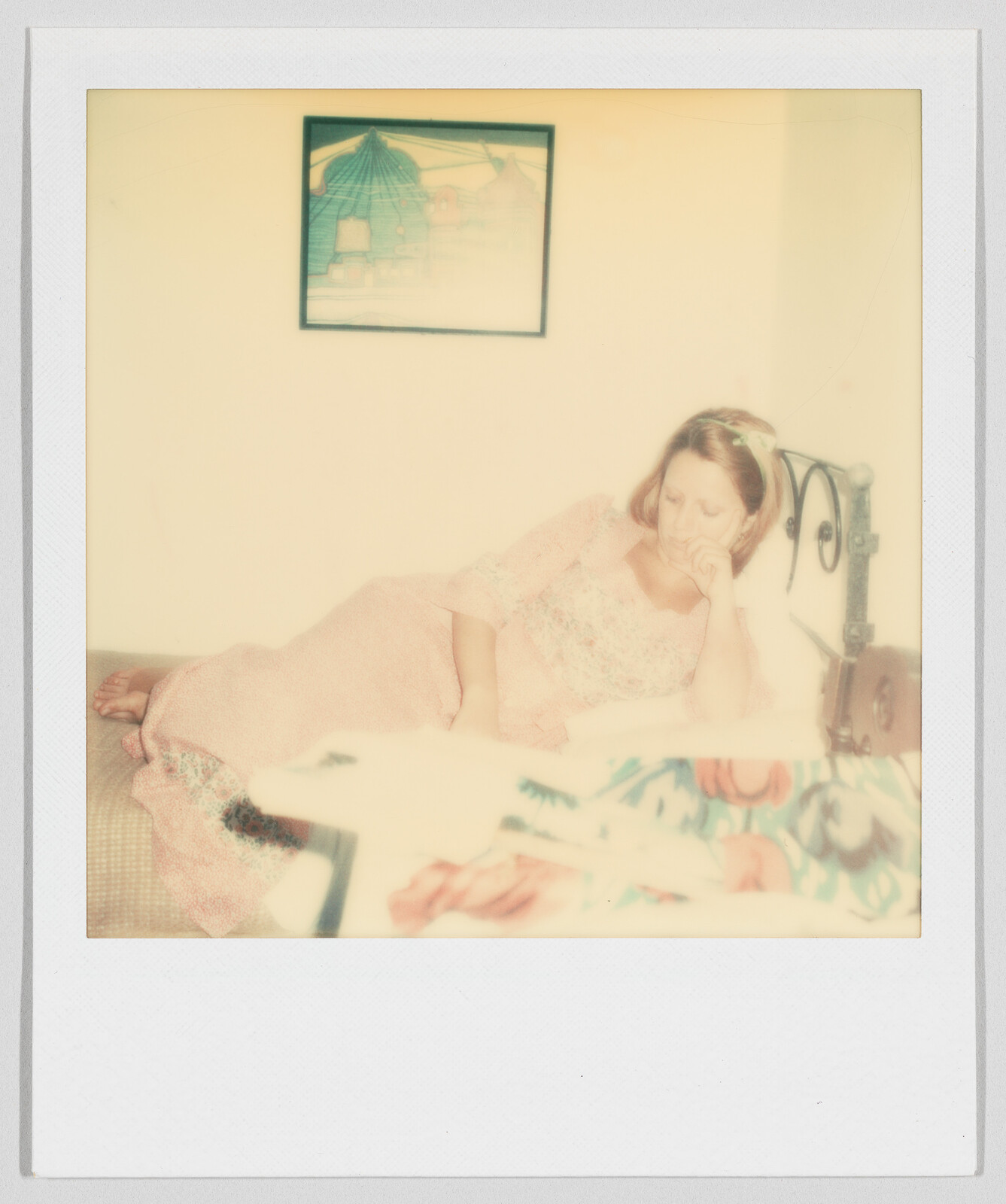 Woman in a pink dress lying on a bed, resting her head on her hand, with a painting above.