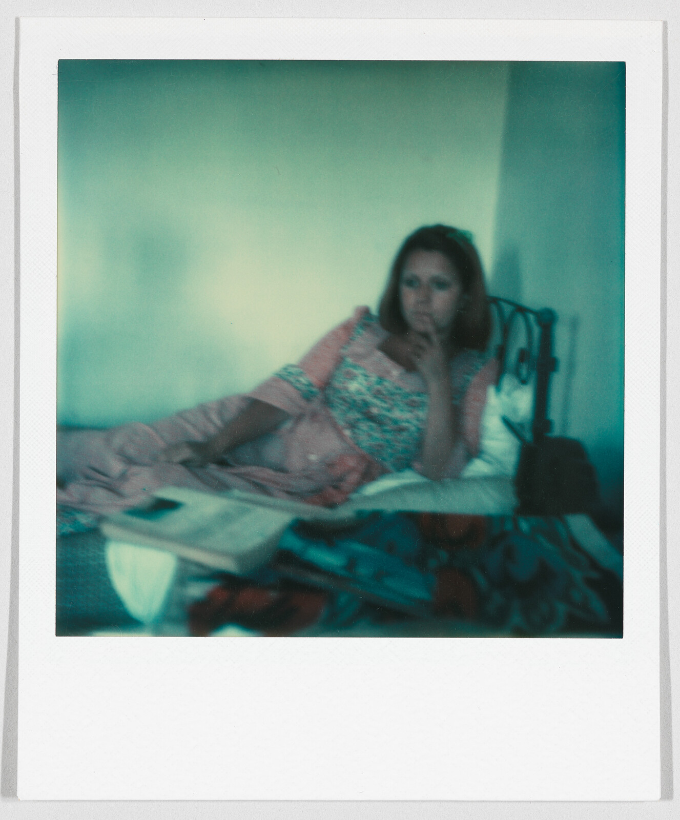 A woman in a patterned dress lies on a bed, resting her head on her hand, looking thoughtful.