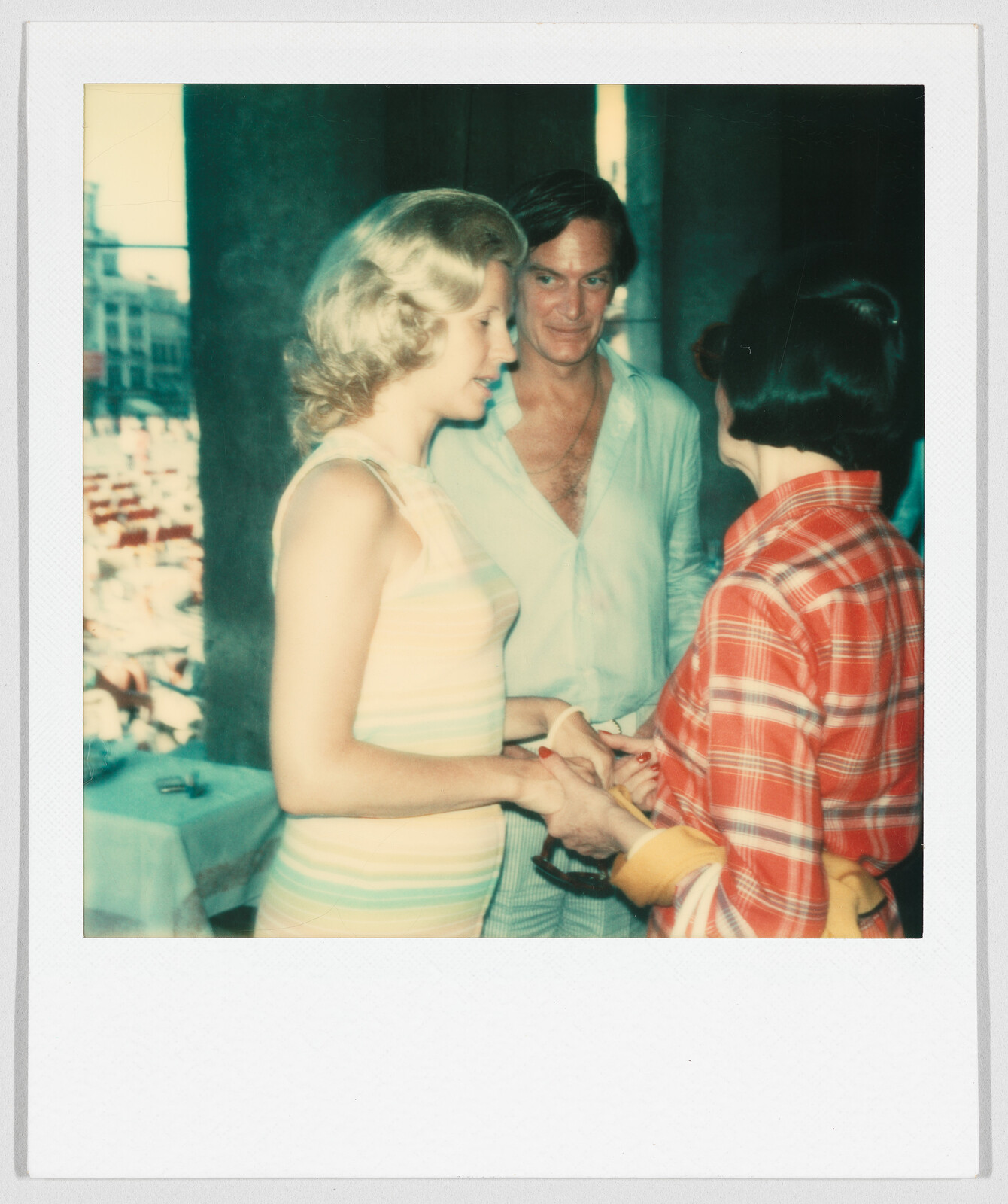 Three people stand together indoors, with two women shaking hands and a man watching them and smiling.