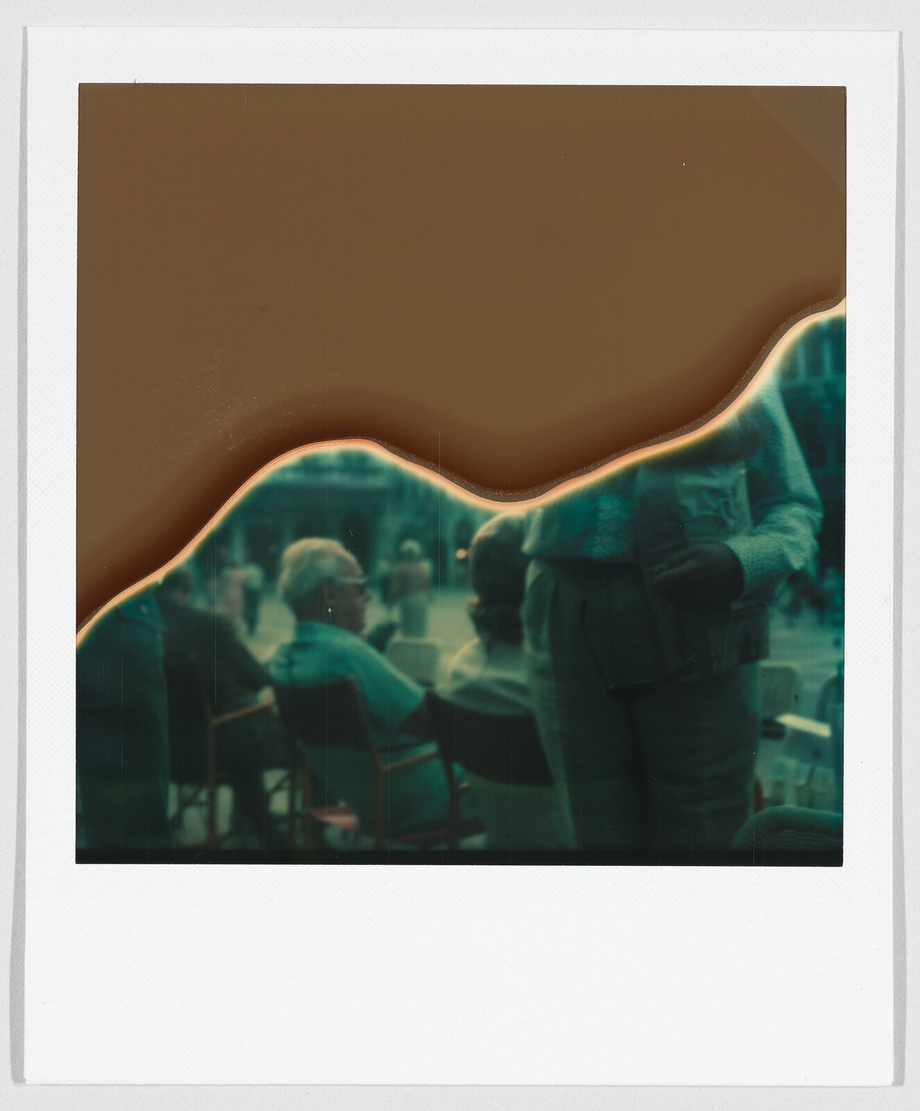 A damaged instant photo shows people sitting outdoors, with a large brown mark covering the top half.