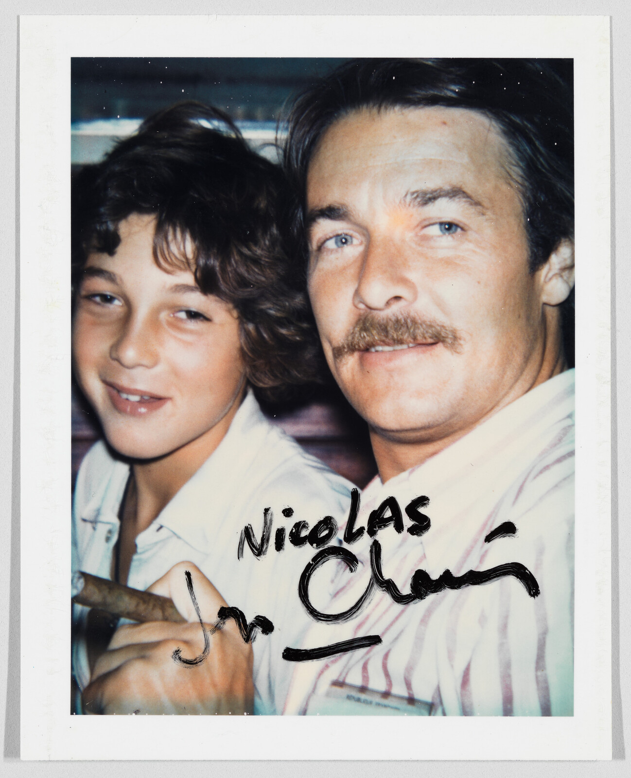 A man with a mustache and a boy smile together; “Nicolas” is handwritten in black marker on the photo.