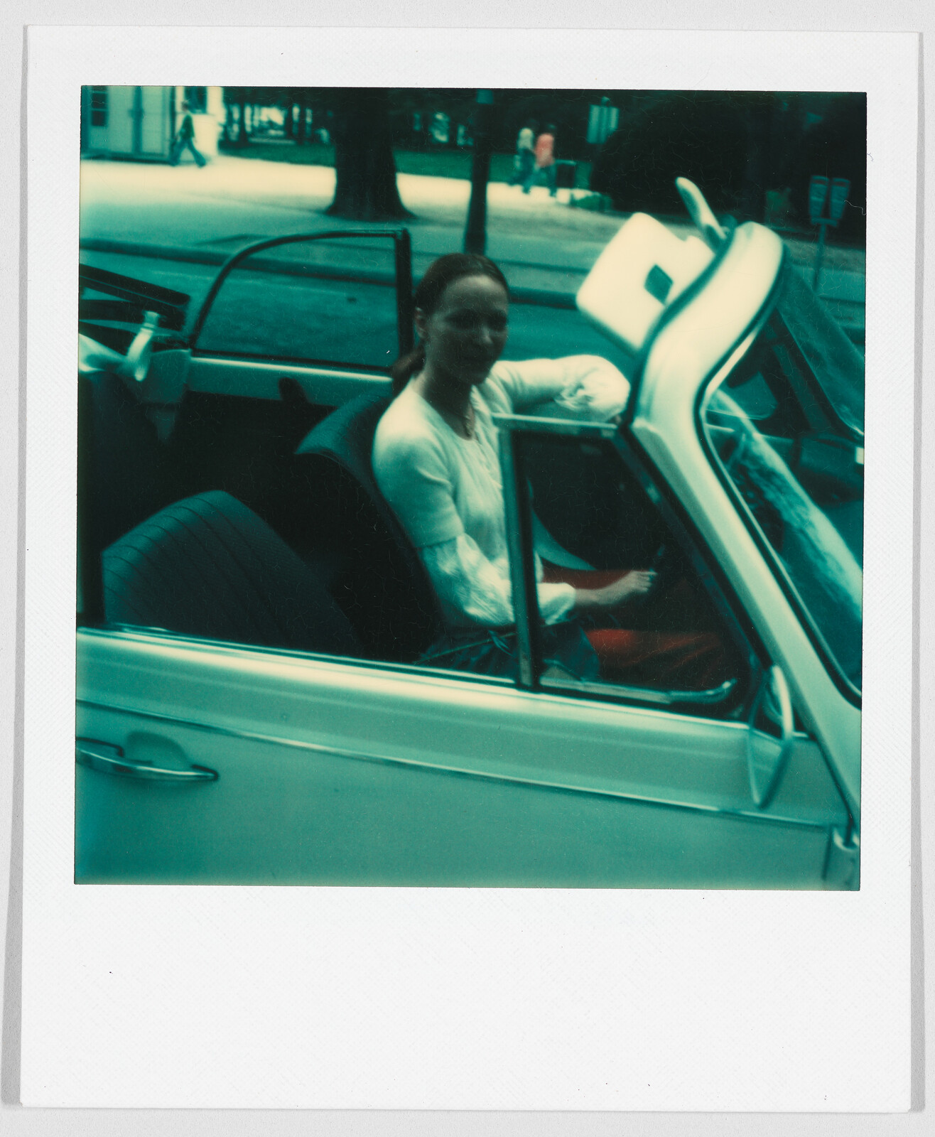 A woman sits in the driver’s seat of a white convertible car with the door open.