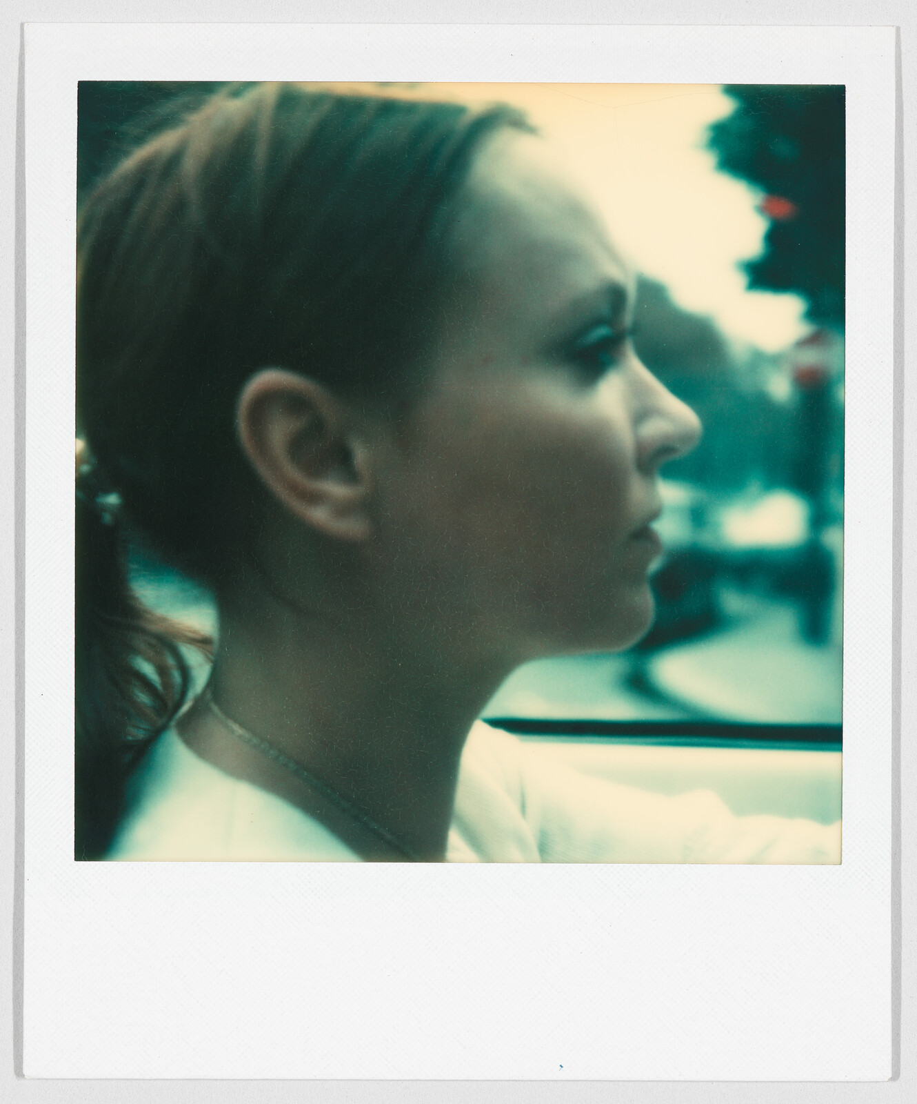 A woman with light brown hair looks forward while driving a car, with a blurred street in the background.