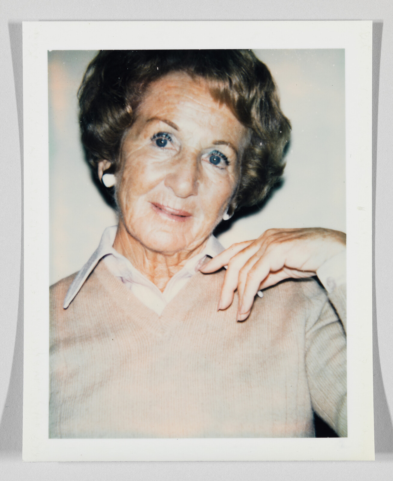 Older woman with short hair and earrings, wearing a light sweater, looks at the camera with a gentle smile.