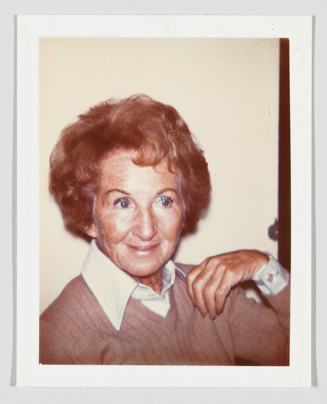 Smiling older woman with short wavy hair resting her hand near her shoulder.