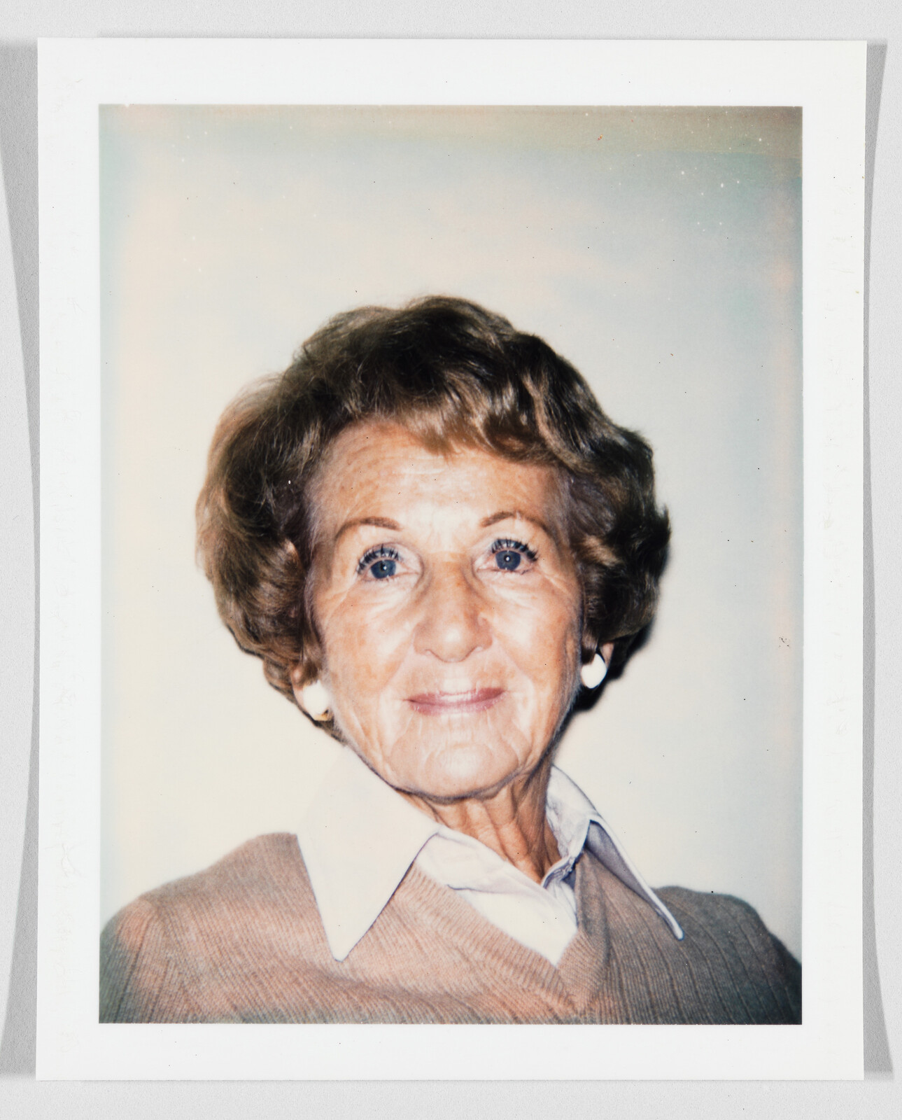 An elderly woman with short hair and a warm smile wearing a collared shirt and sweater.