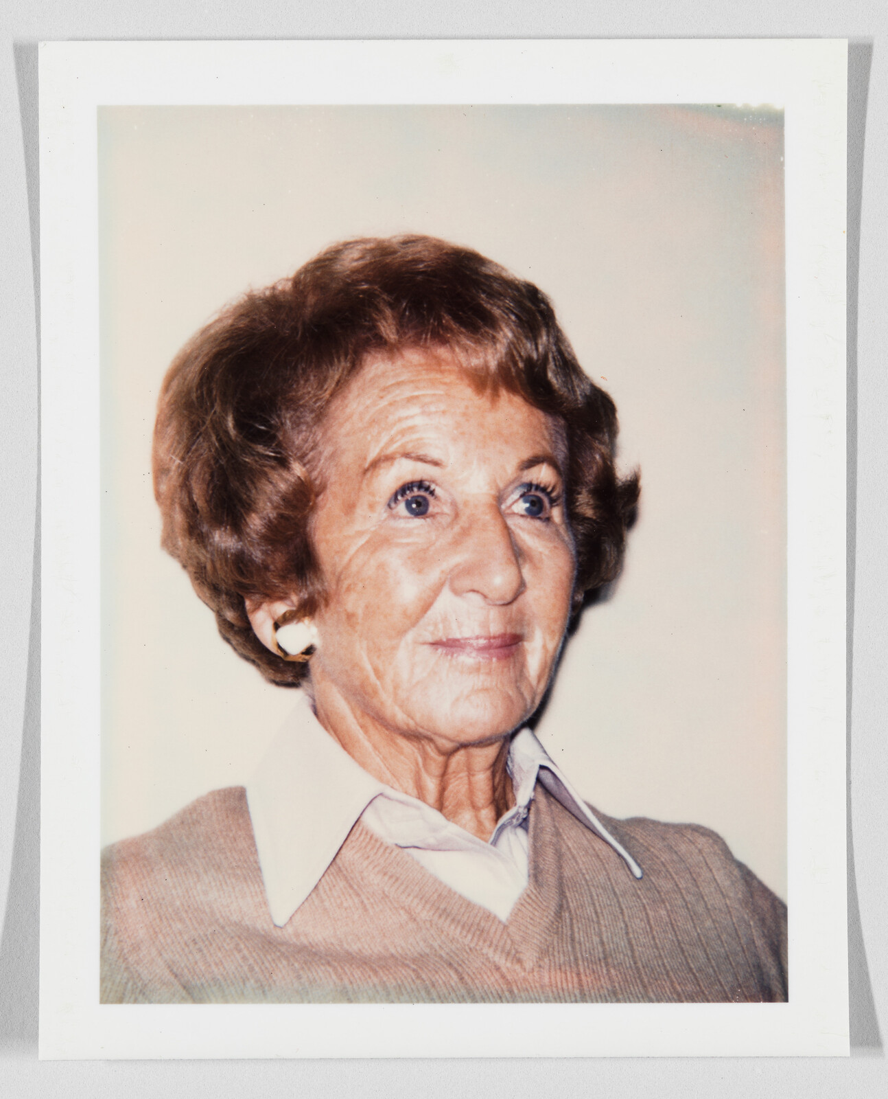 Elderly woman with short brown hair and white earrings looks slightly upward with a calm expression.