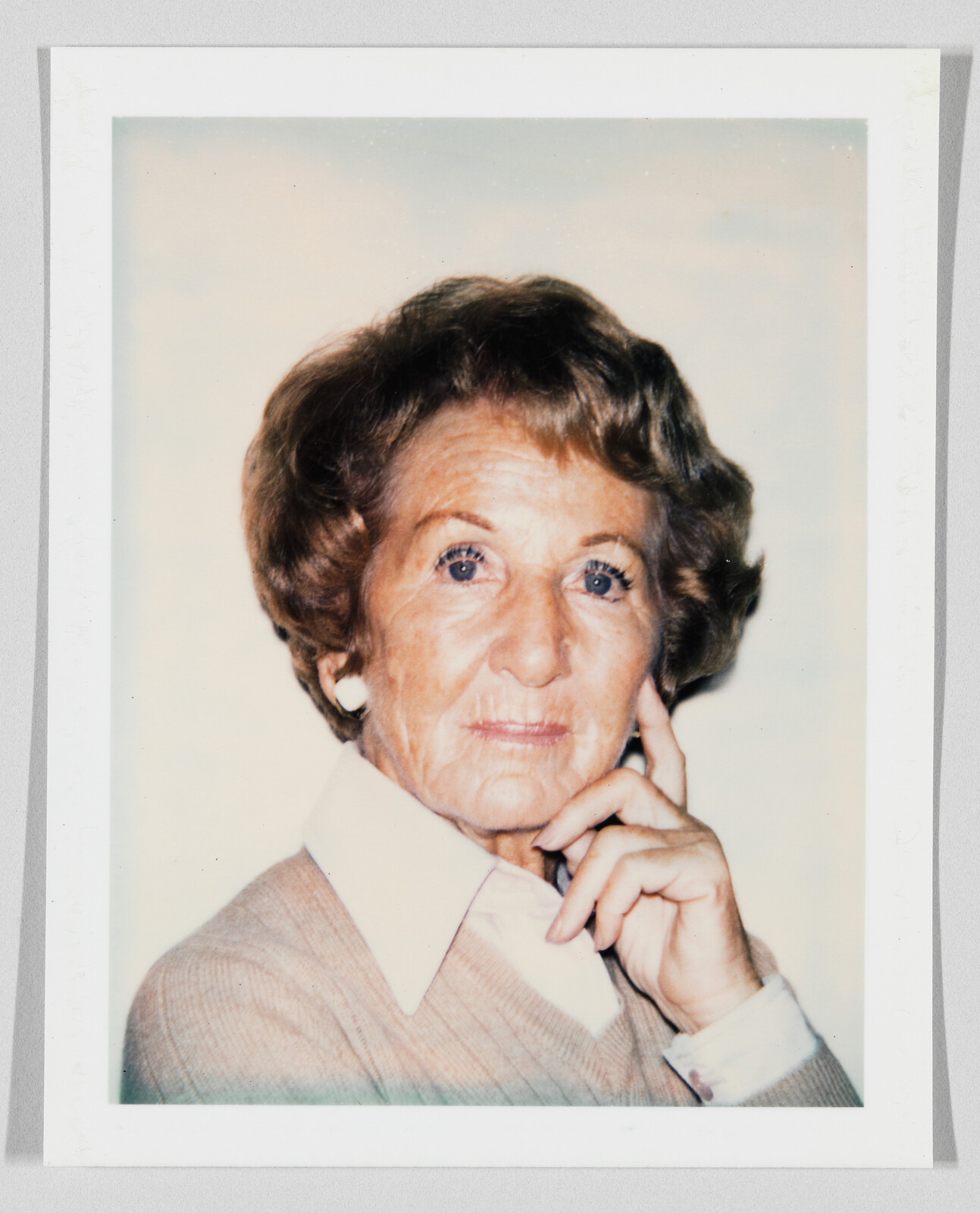 Older woman with short brown hair and earrings, resting her chin on her hand, looking at the camera.
