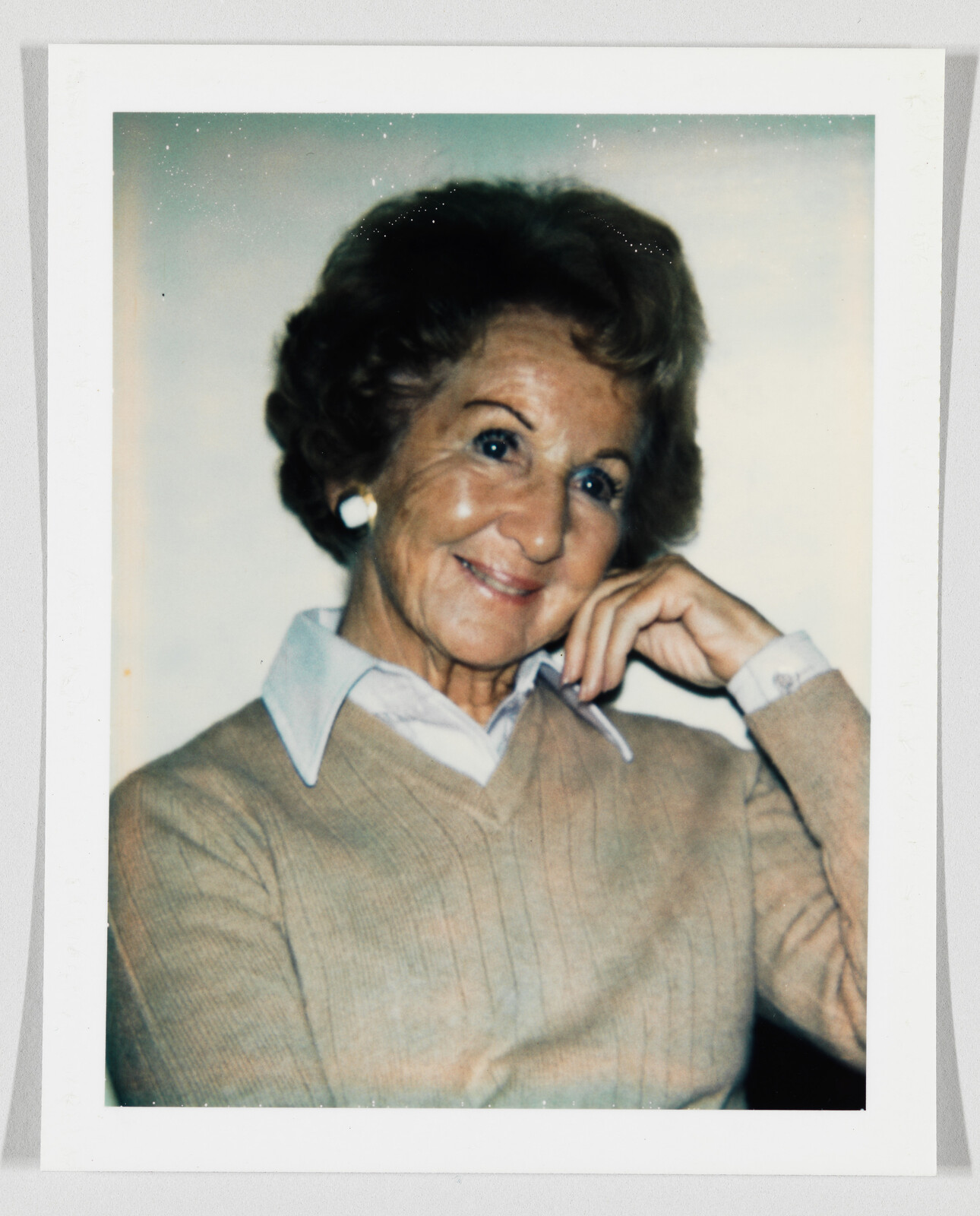 Elderly woman smiling warmly while resting her chin on her hand.