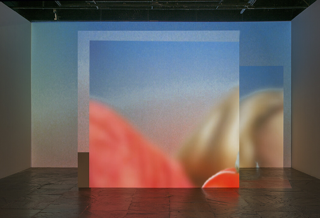 Large blurred colorful projection fills a dark gallery, overlapping rectangular panels on the floor and walls.