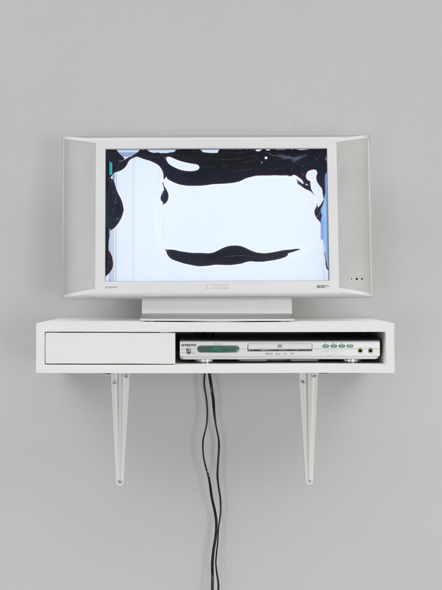 A wall-mounted white TV with a distorted black-and-white screen above a shelf and dangling cables.