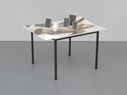 A square table with a glossy photo surface holds a small white vase and five small framed panels.