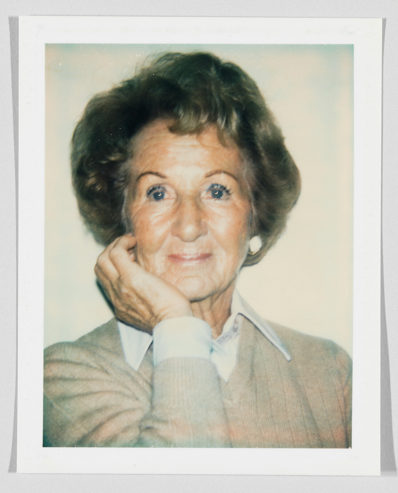 Elderly woman with short hair resting her chin on her hand and smiling softly.
