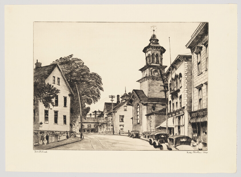 A quiet main street lined with buildings and vintage cars leading to a tall church tower.