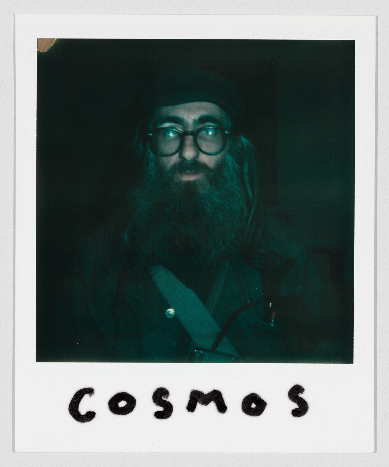 Bearded man with glasses and hat stares into camera with "COSMOS" written below.