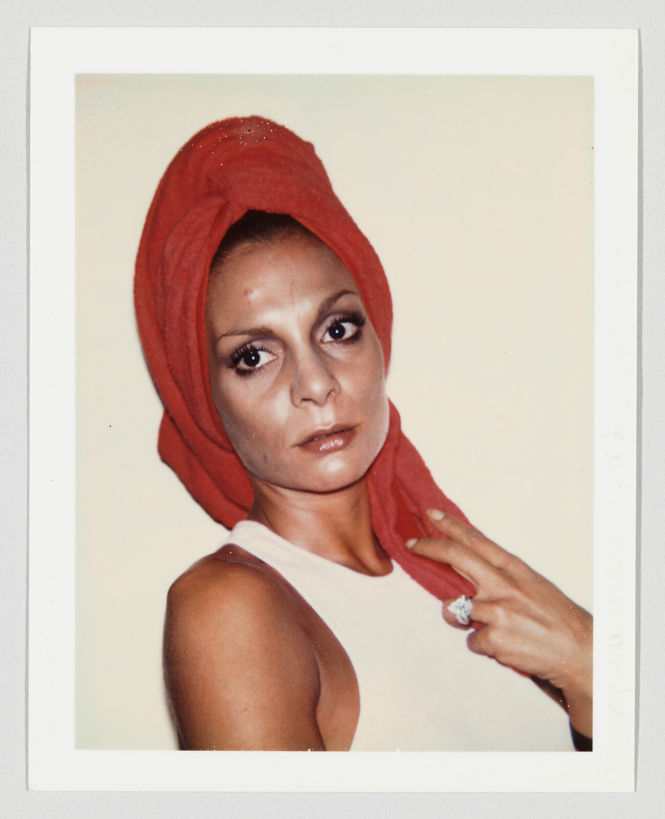 Woman wearing a red towel wrapped around her head looks toward camera while holding the fabric and ring.
