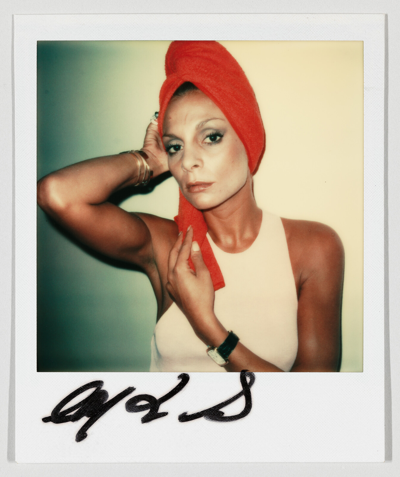 Woman wearing a red towel turban adjusts it while looking directly at the camera.