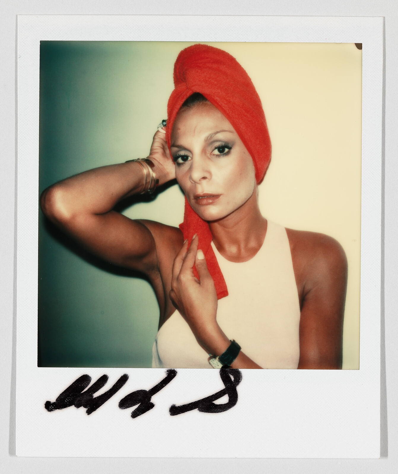 Woman with a red towel wrapped around her head adjusts it while looking directly at the camera.