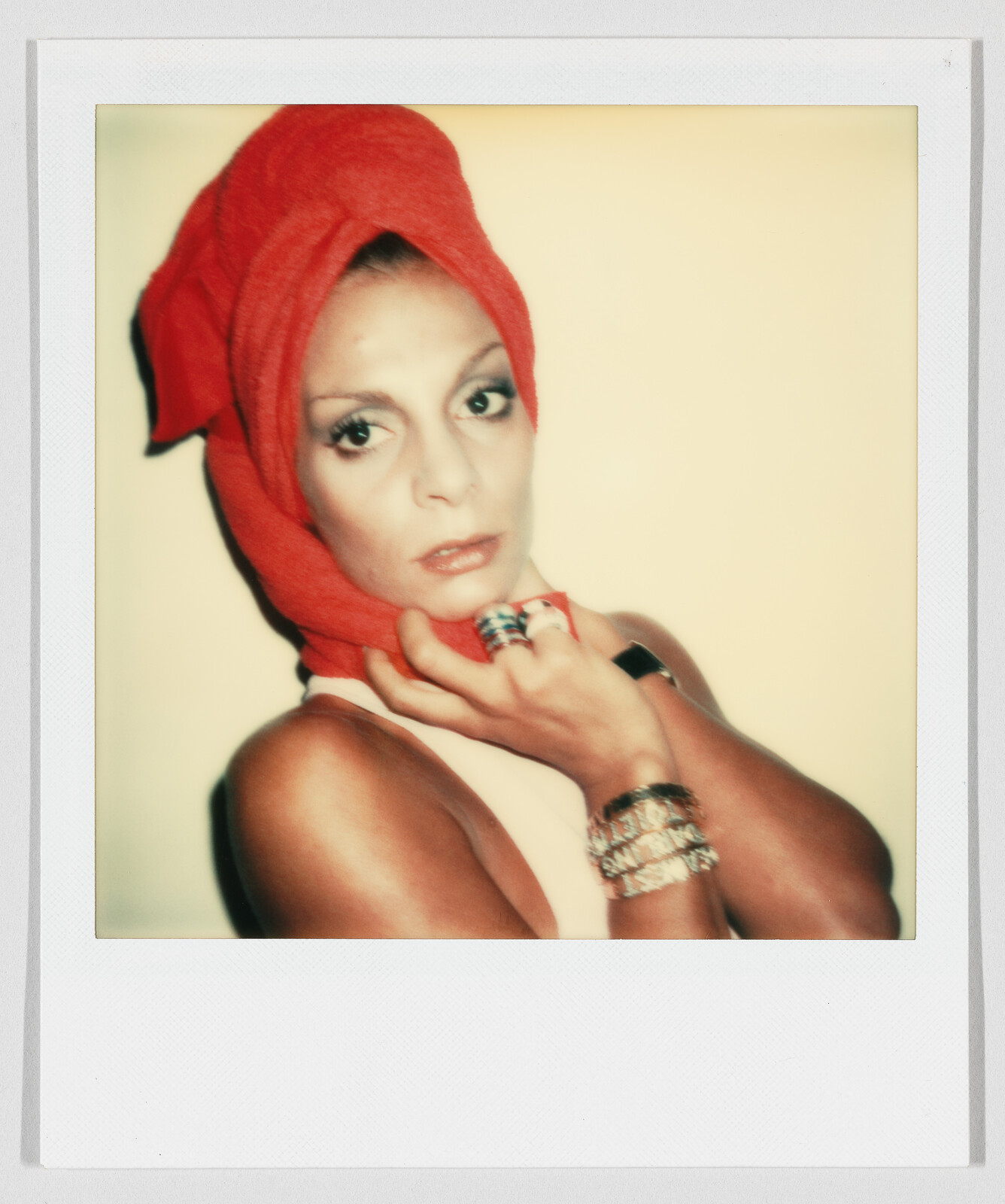 Woman wearing a red towel turban looks at camera with hand near face showing rings and bracelets.