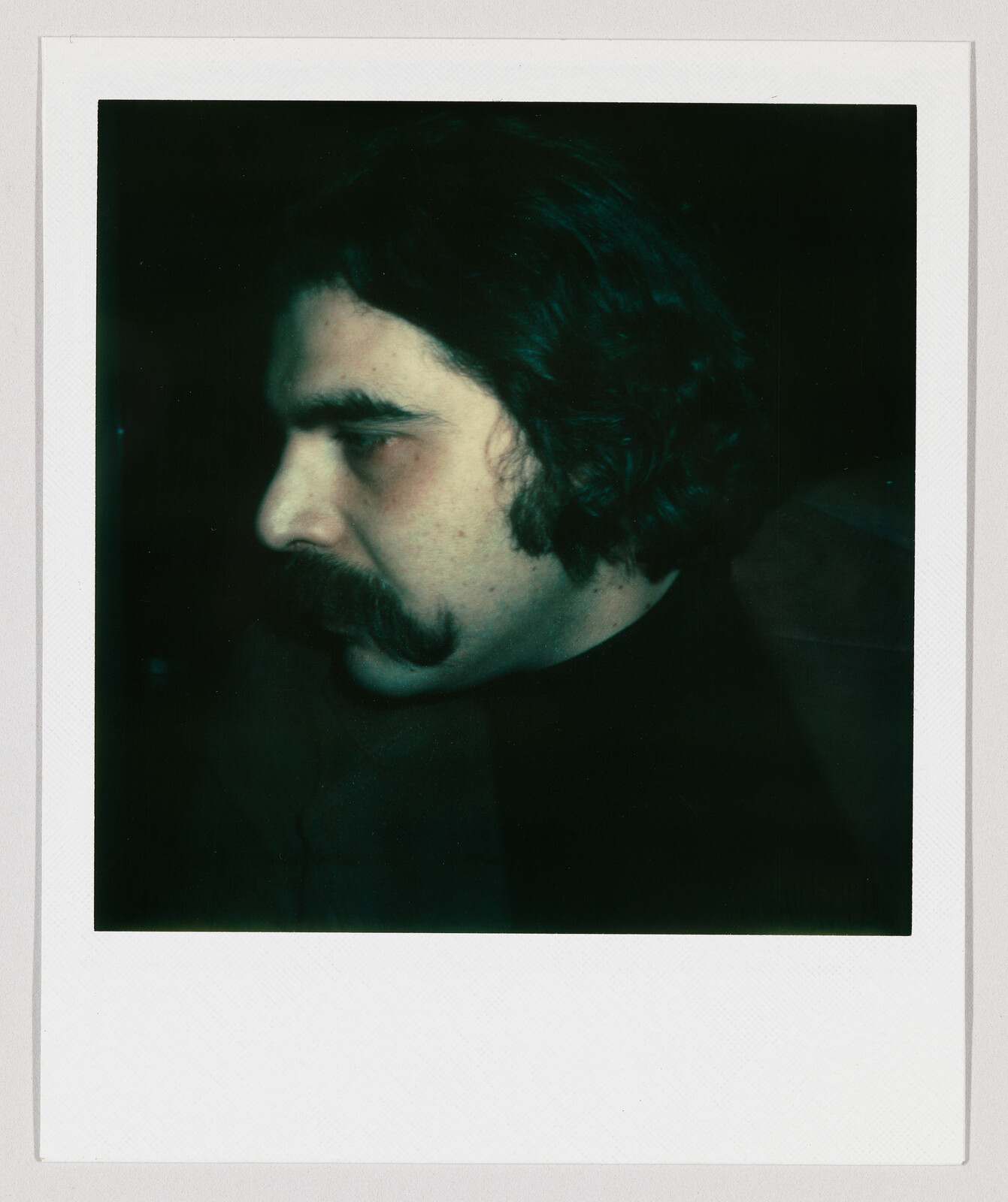 A man with dark hair and a thick curled mustache shown in a close side profile.