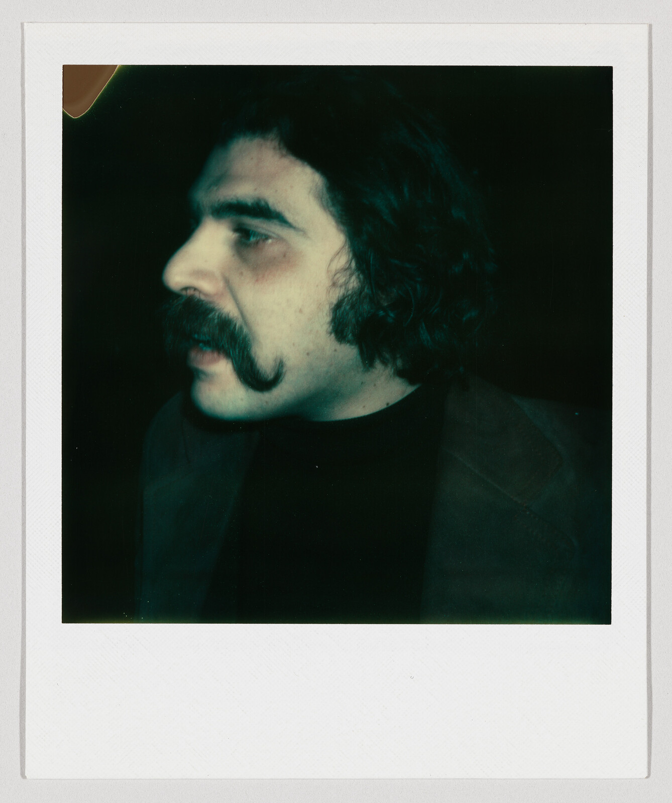 Man with thick curled mustache and sideburns looking to the left against a dark background.