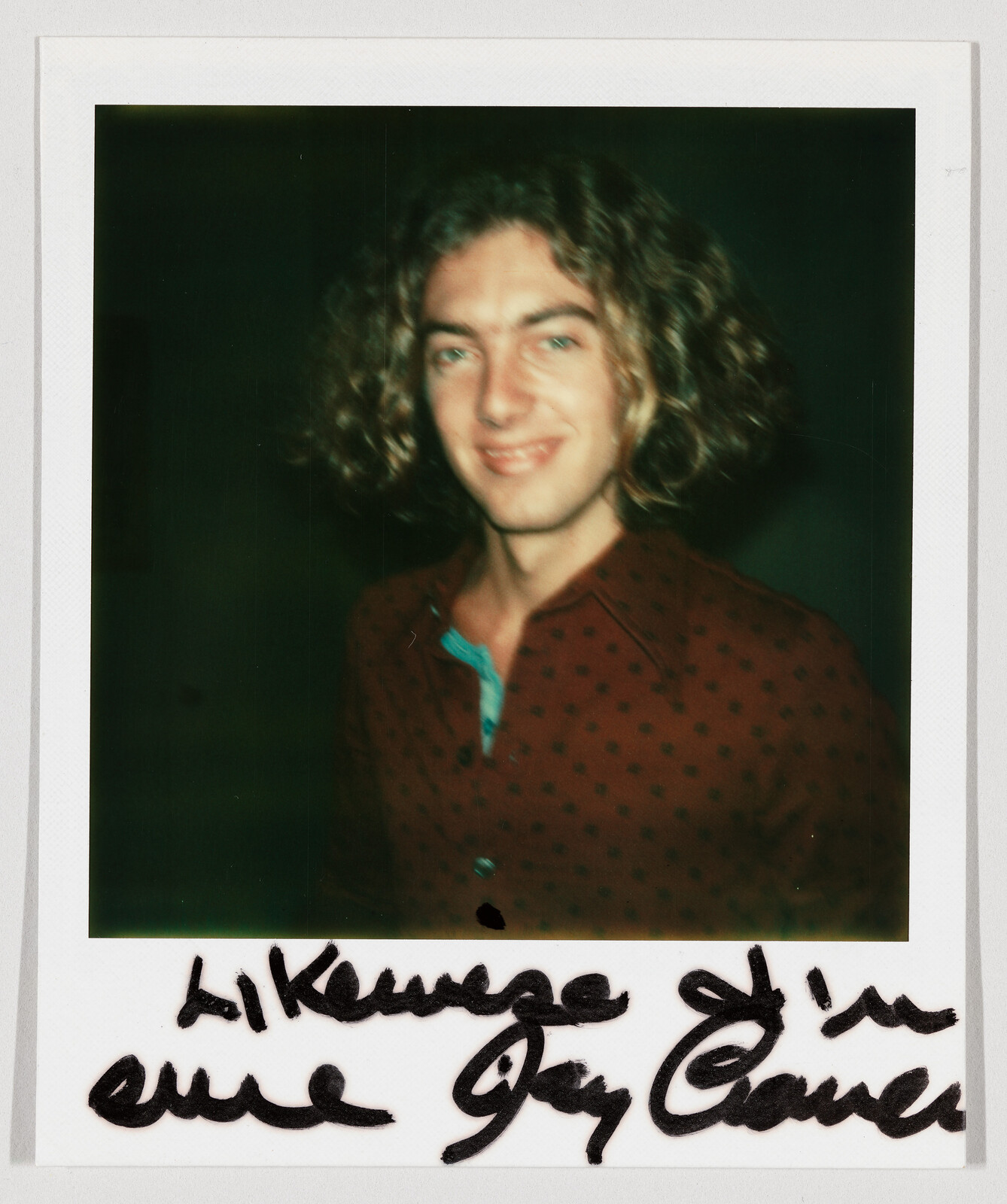 Young person with curly hair smiling in a Polaroid photograph with handwritten text below.