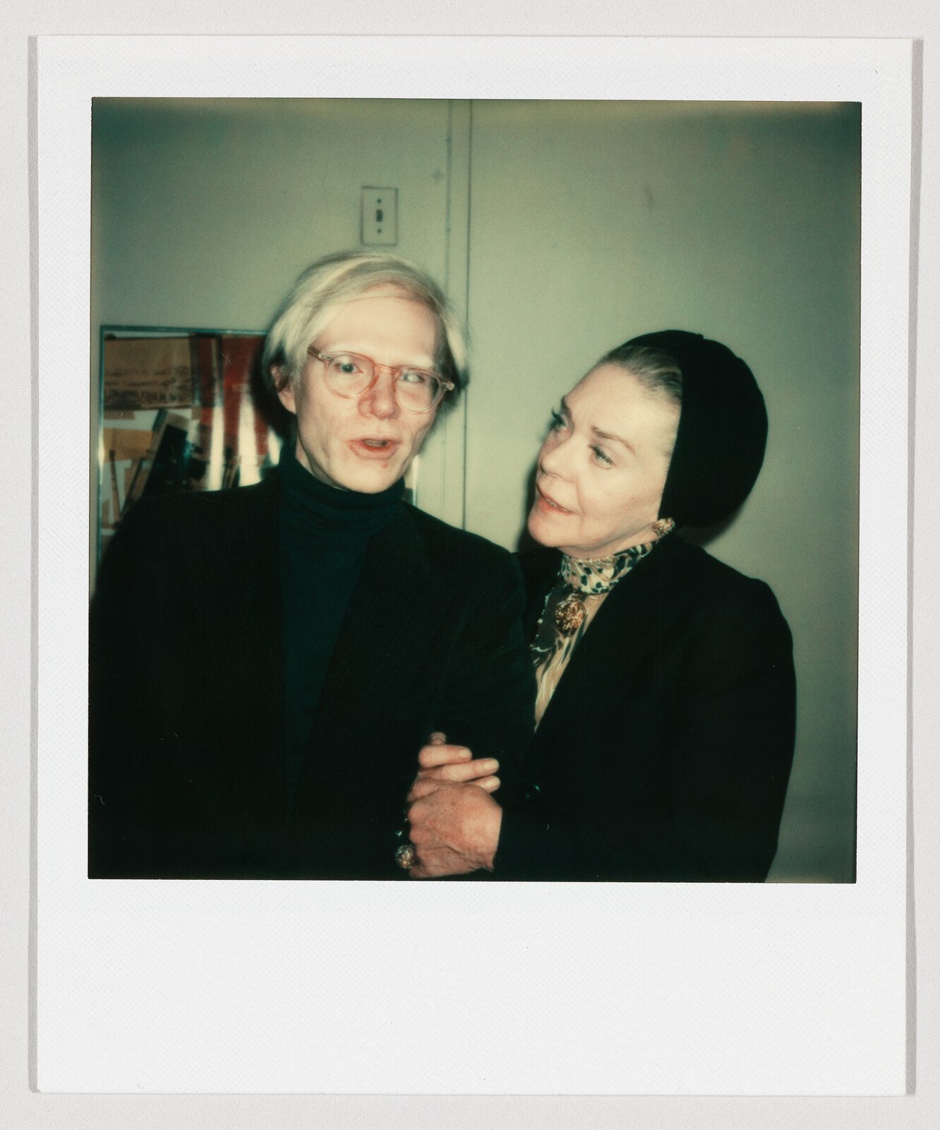 A man with glasses speaks while a woman in a headscarf holds his arm and listens.