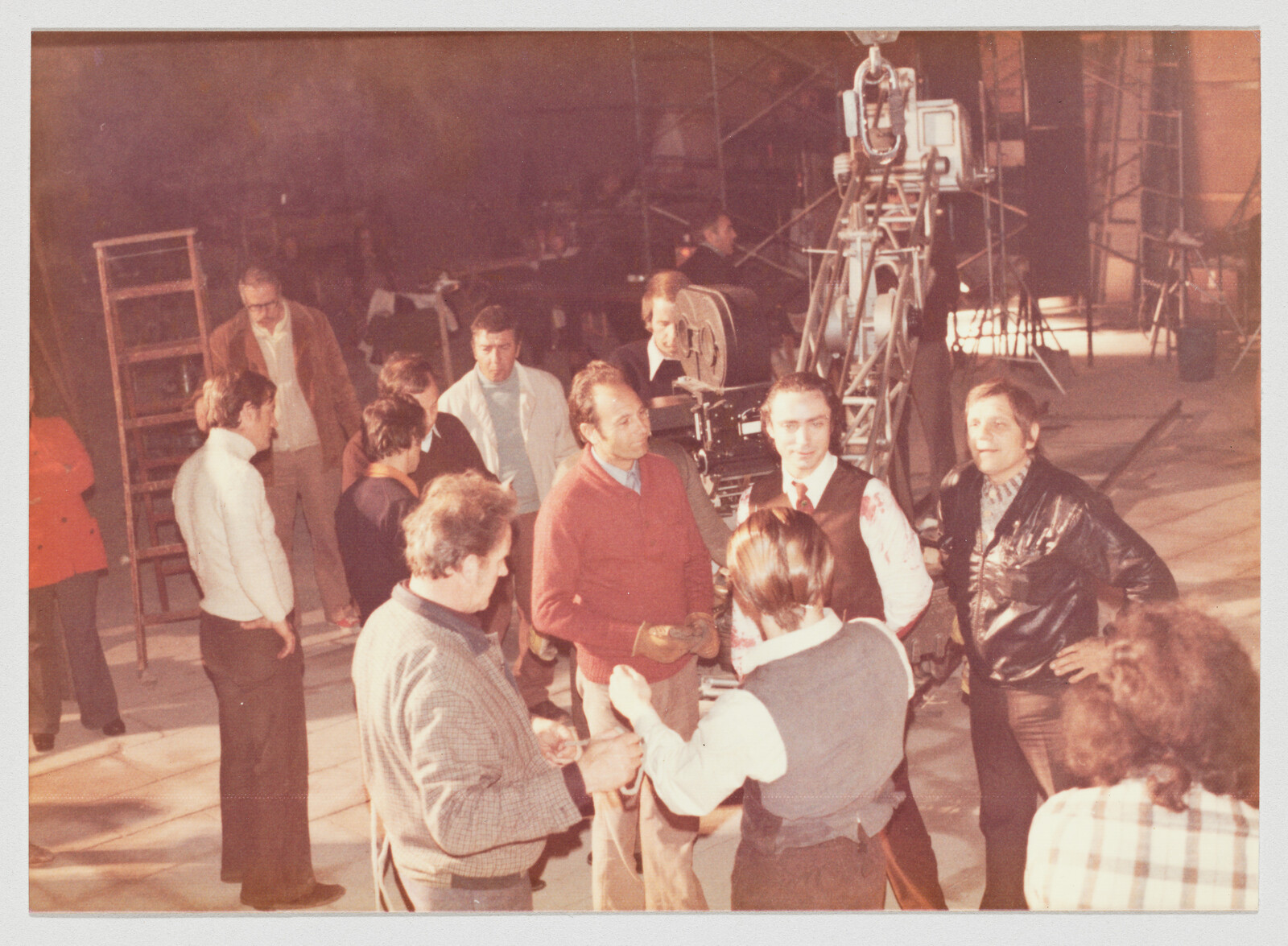 Film crew clustered around a large camera and lighting rig, talking and preparing a shot.