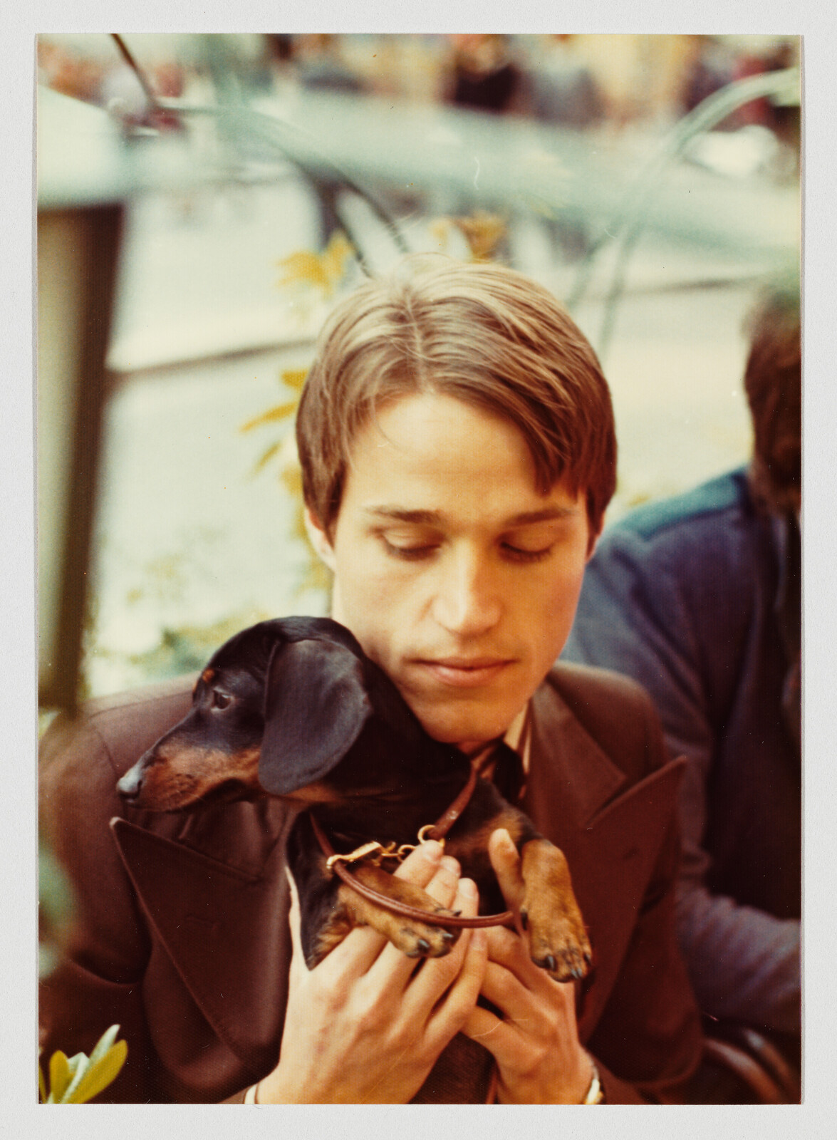A young man gently holds a small dachshund against his chest, looking down.