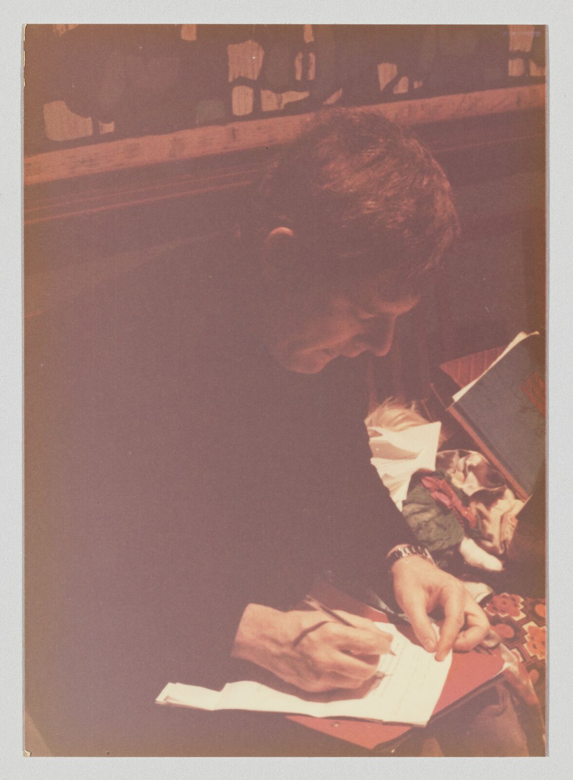 A person leans over and writes on a sheet of paper with a pen.