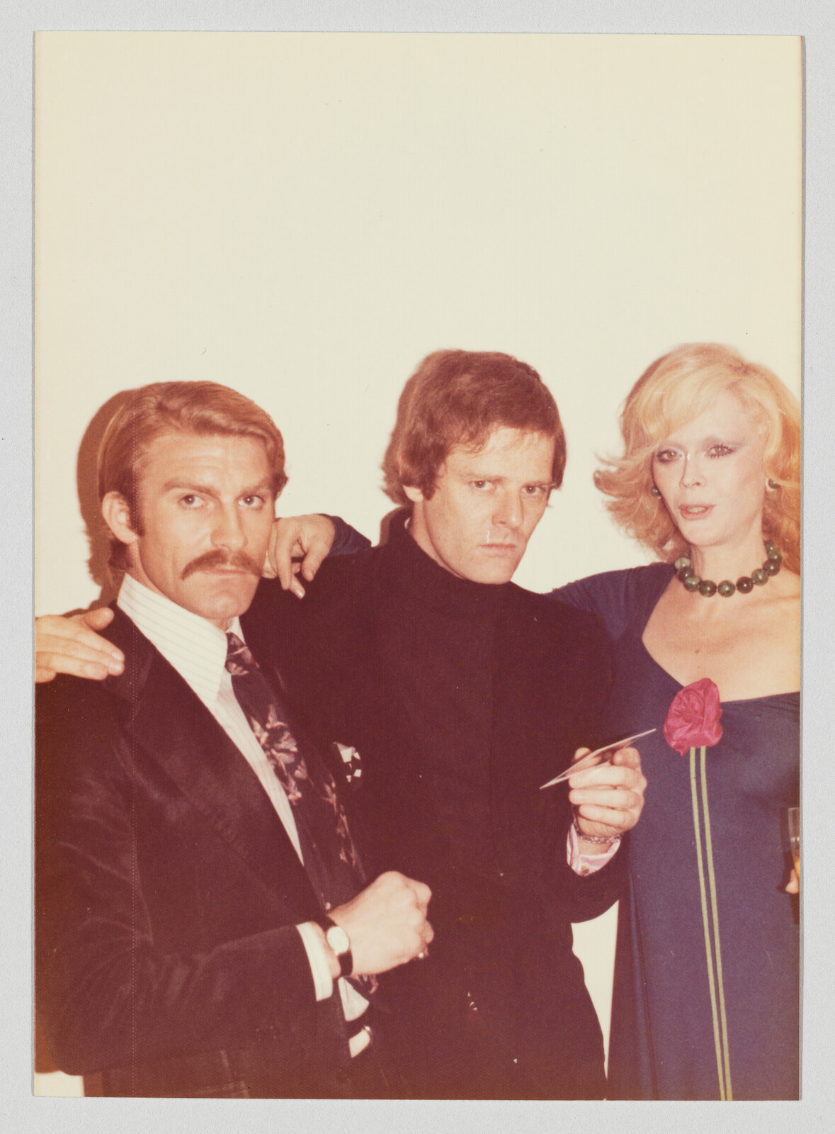 Three adults pose together at a party, the man in the center holding a cigarette.