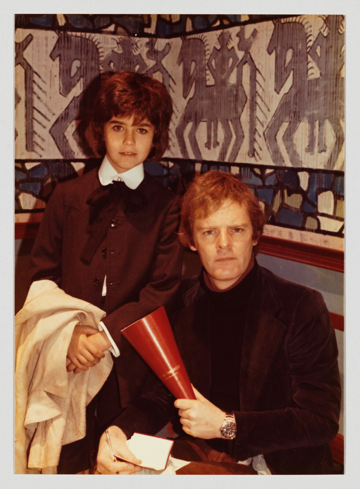 A man holds a red megaphone while a young person stands beside him holding a coat.