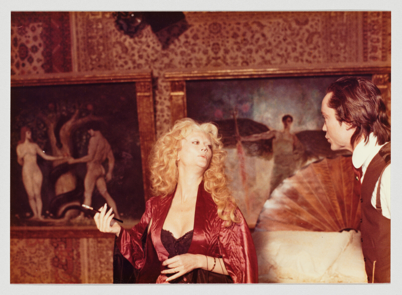 A woman in a red robe holds a cigarette holder while staring dismissively at a man.