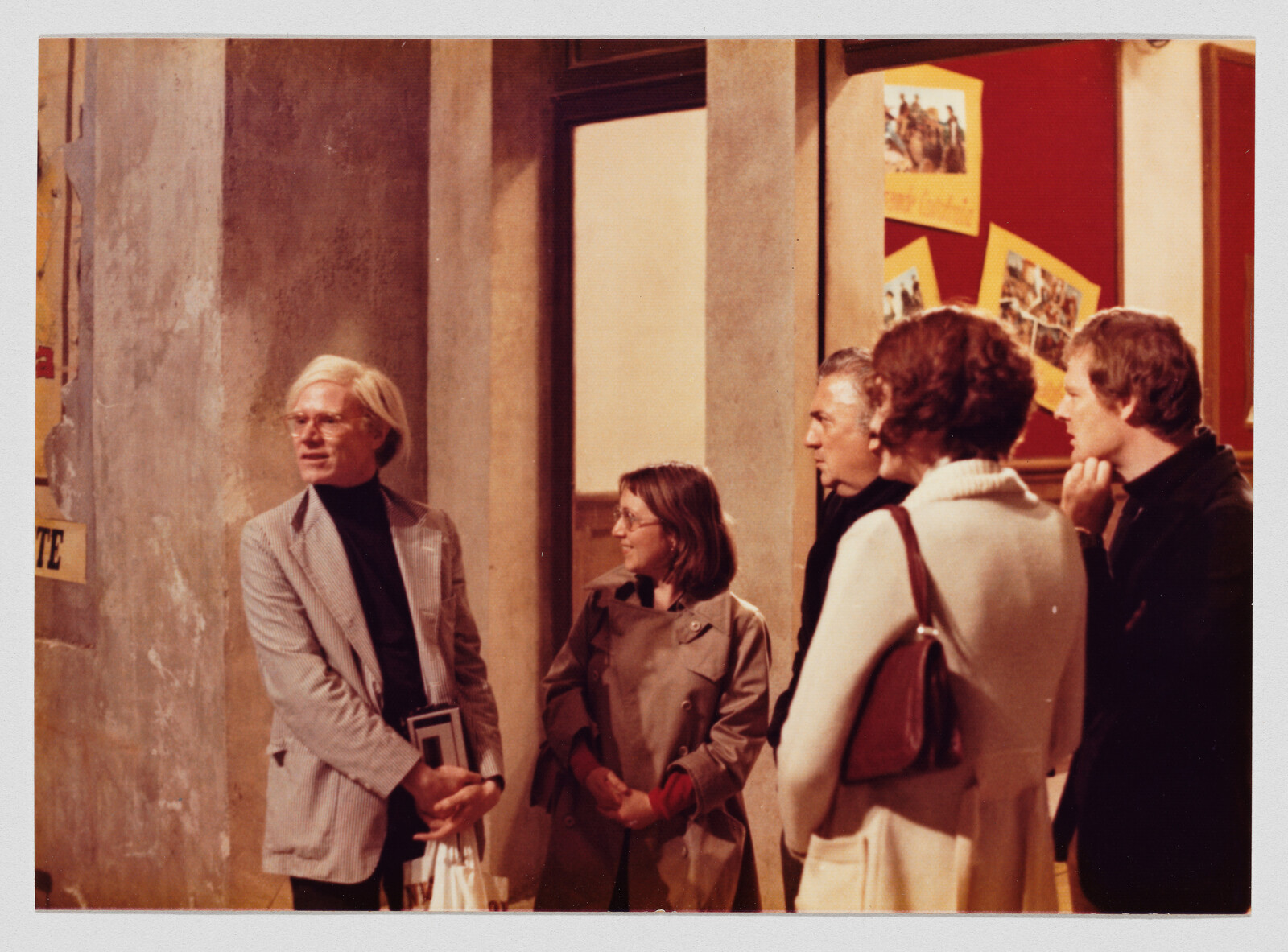 Older man with light hair talks while four people listen in a gallery-like space.