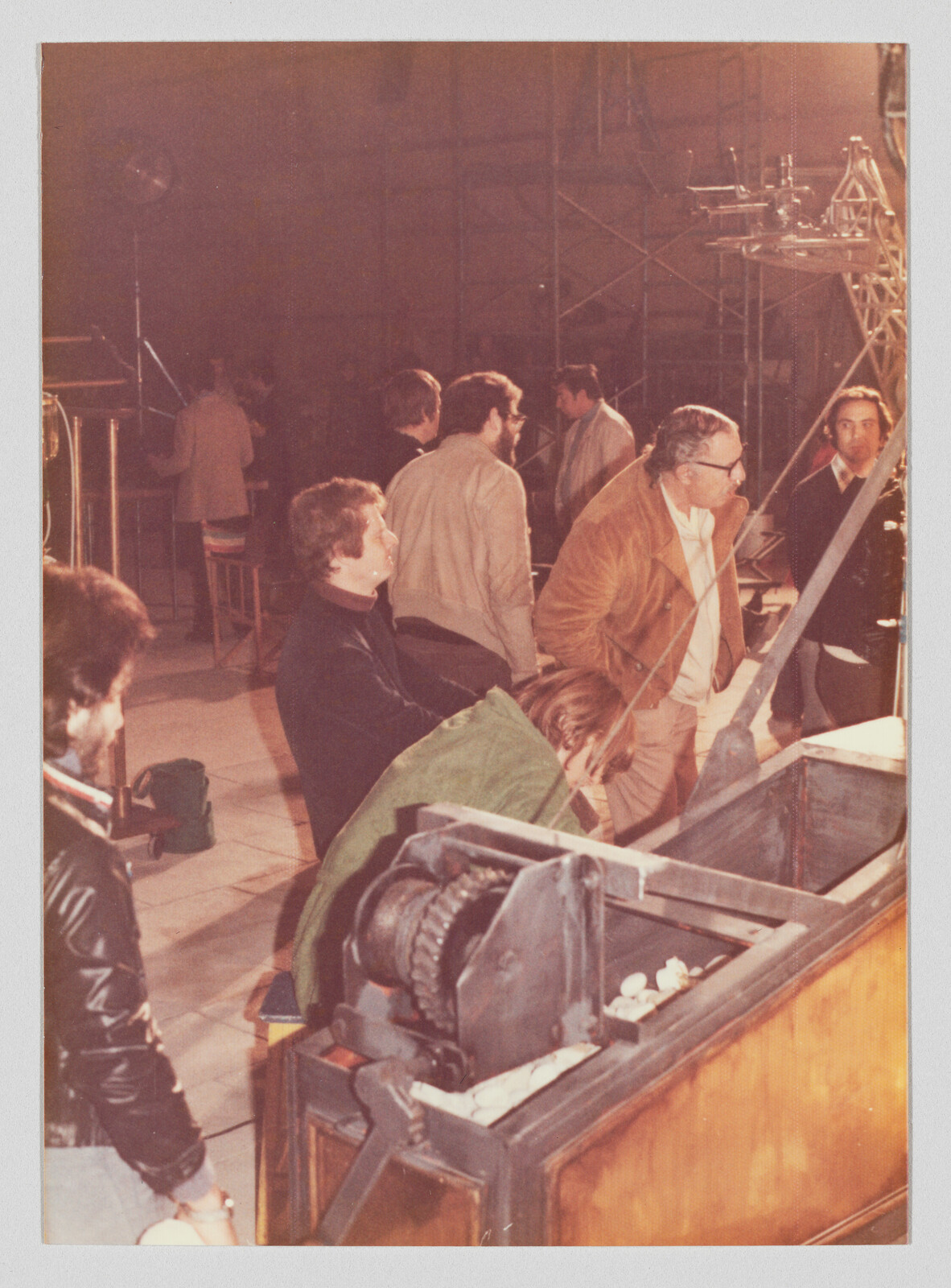 Several men gather around a large mechanical winch and wooden crate, examining the equipment.