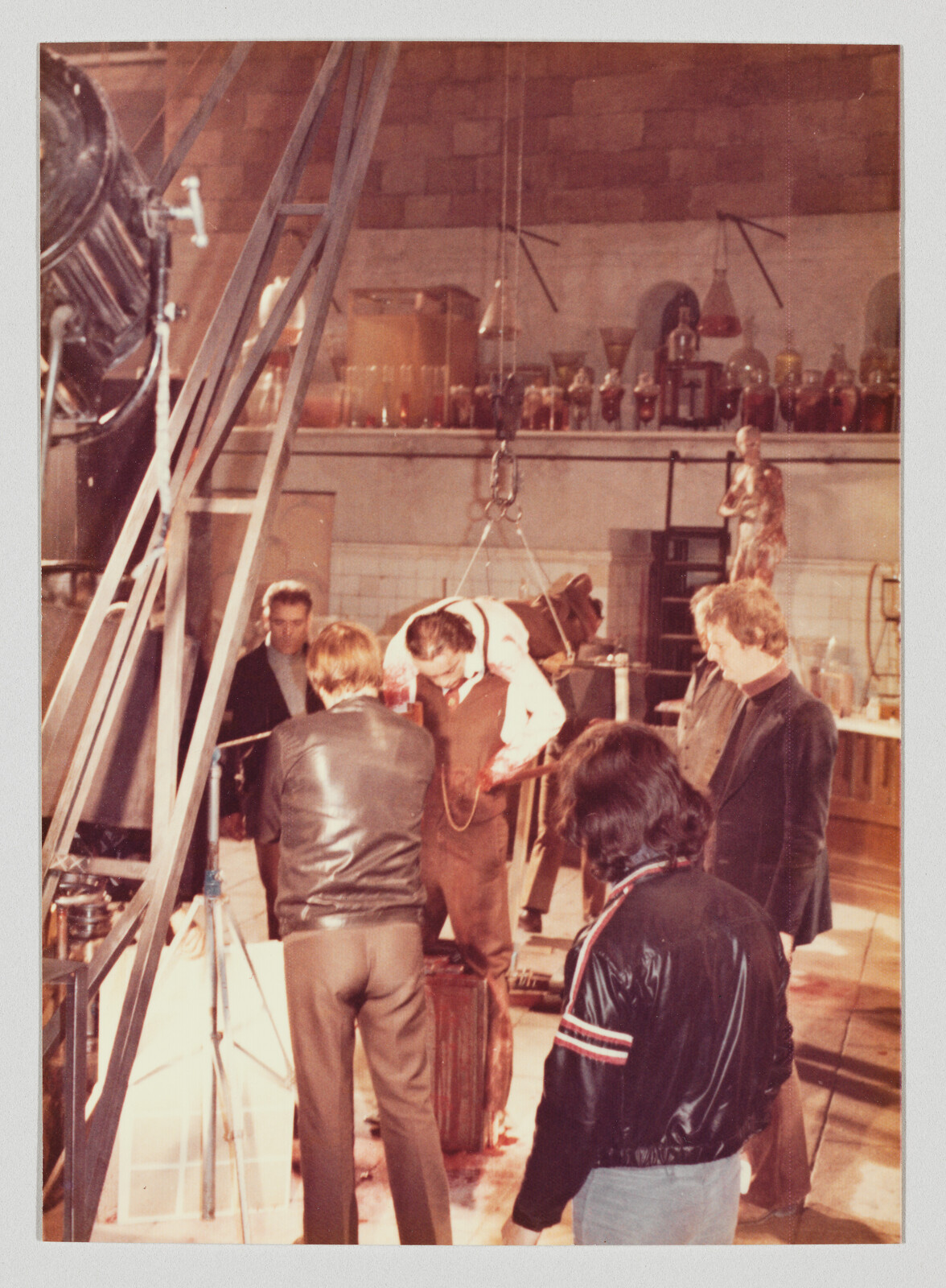 Film crew surrounds a suspended actor in a harness while technicians adjust rigging on set.