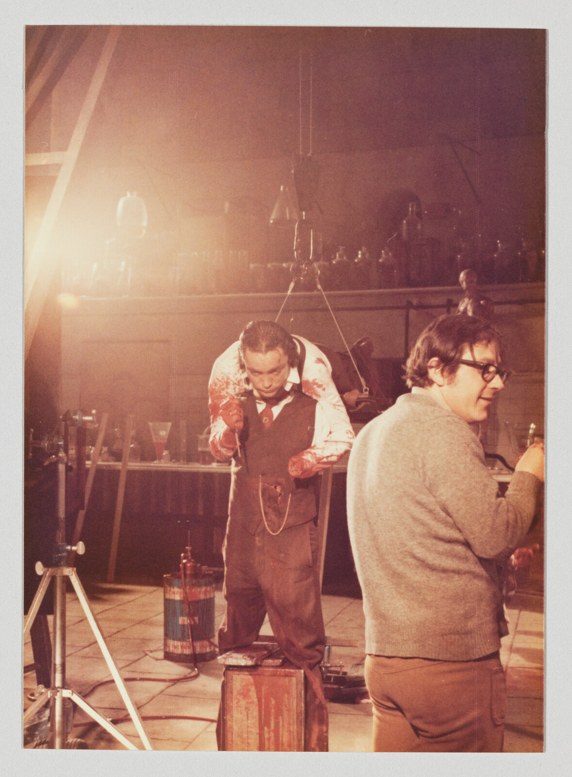 Man with bloodstained sleeves standing on a box while another crew member works nearby.
