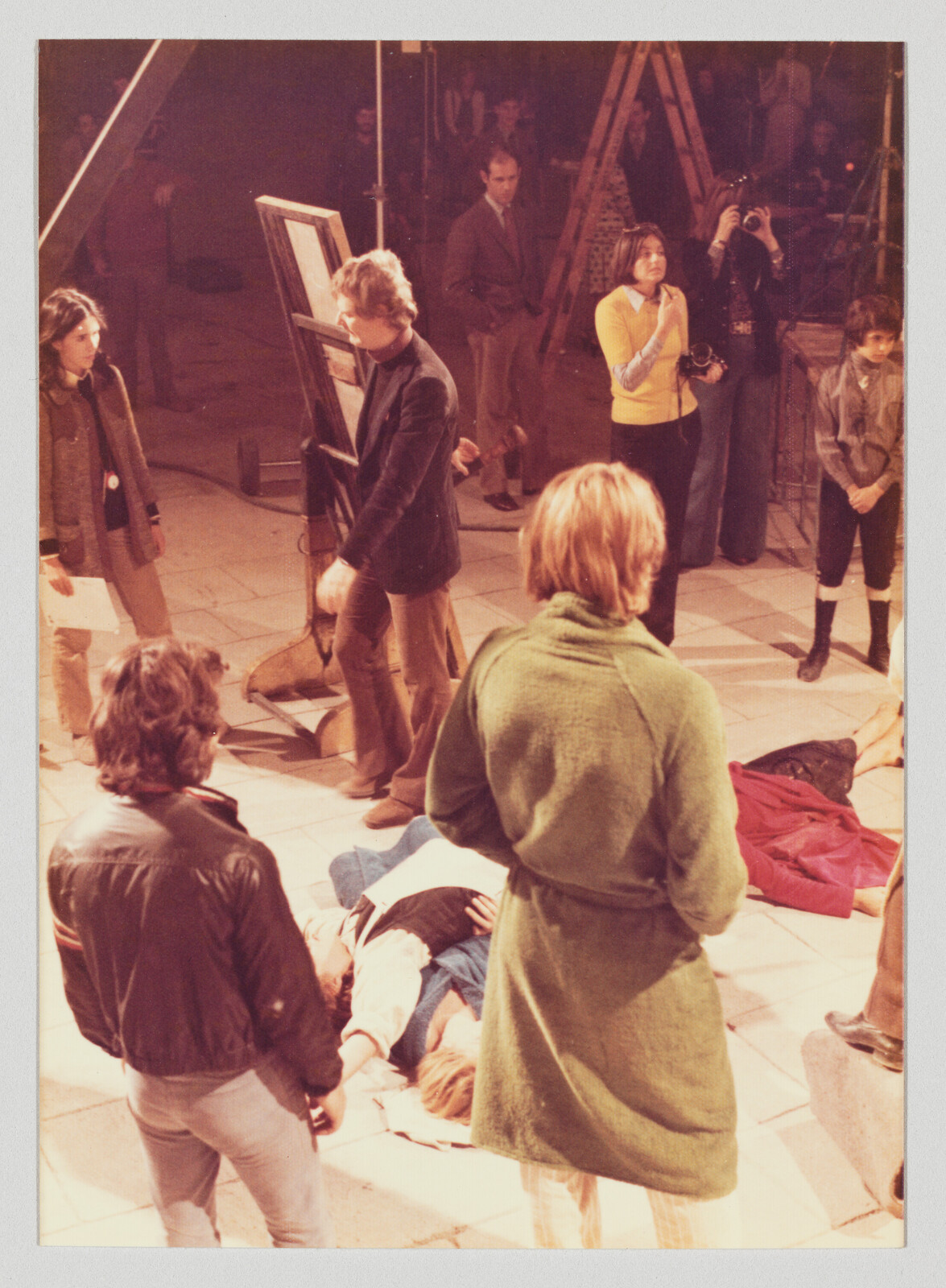 People stand around two people lying on the floor while a photographer takes pictures.