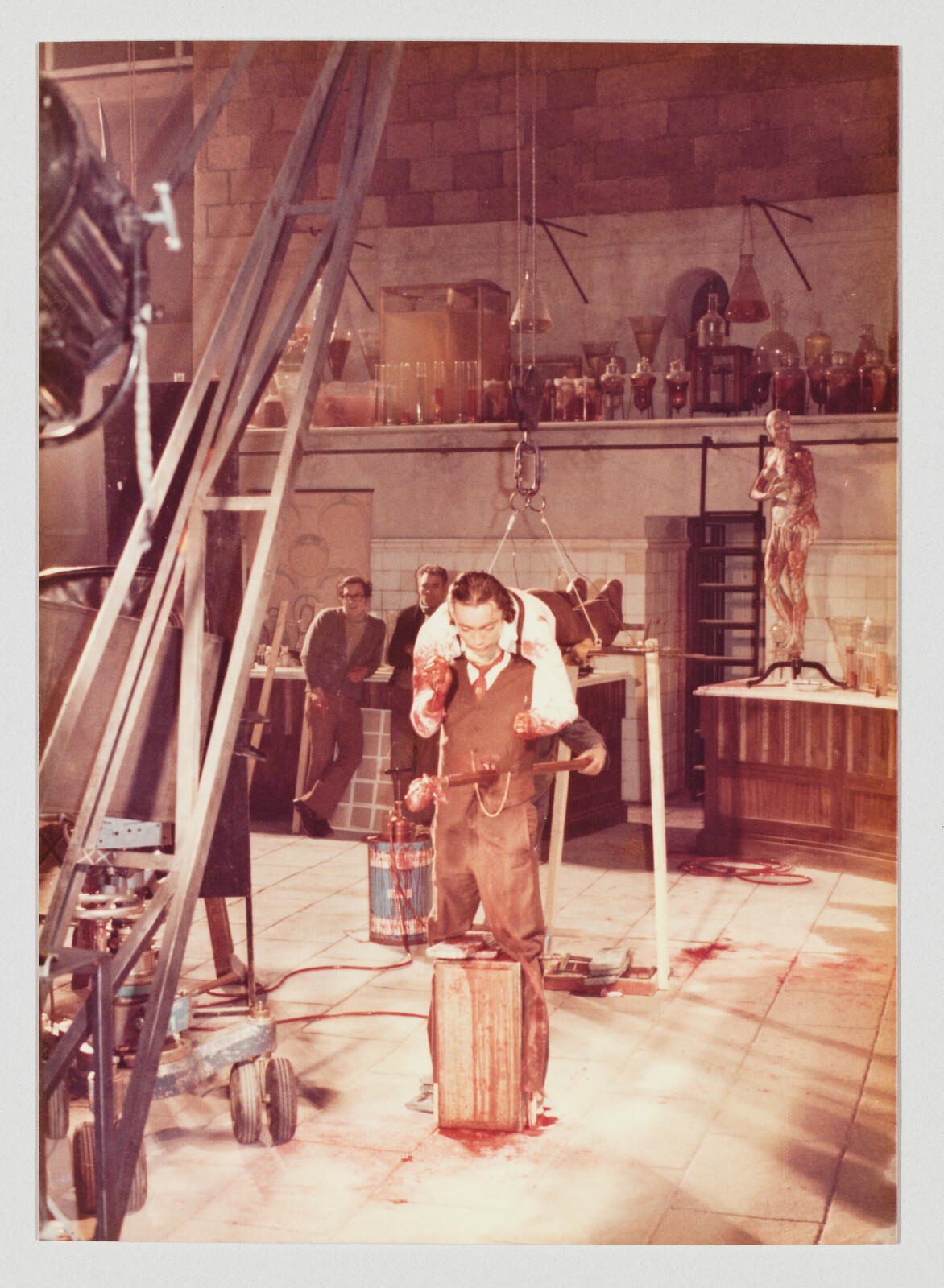 Man in a lab carries a bloody body over his shoulders while blood stains the tiled floor.