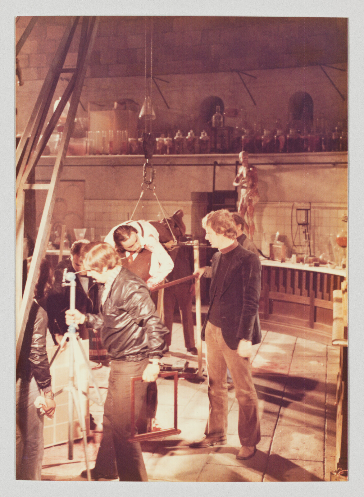 Several crew members adjust a harness and rigging to hoist an actor on a film set.