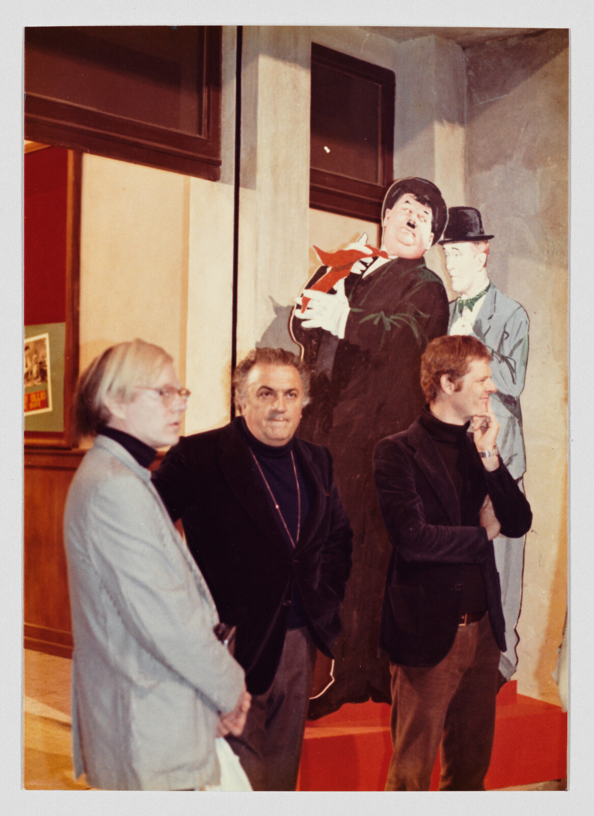 Three men stand in front of a tall painted cutout of two cartoonish figures.
