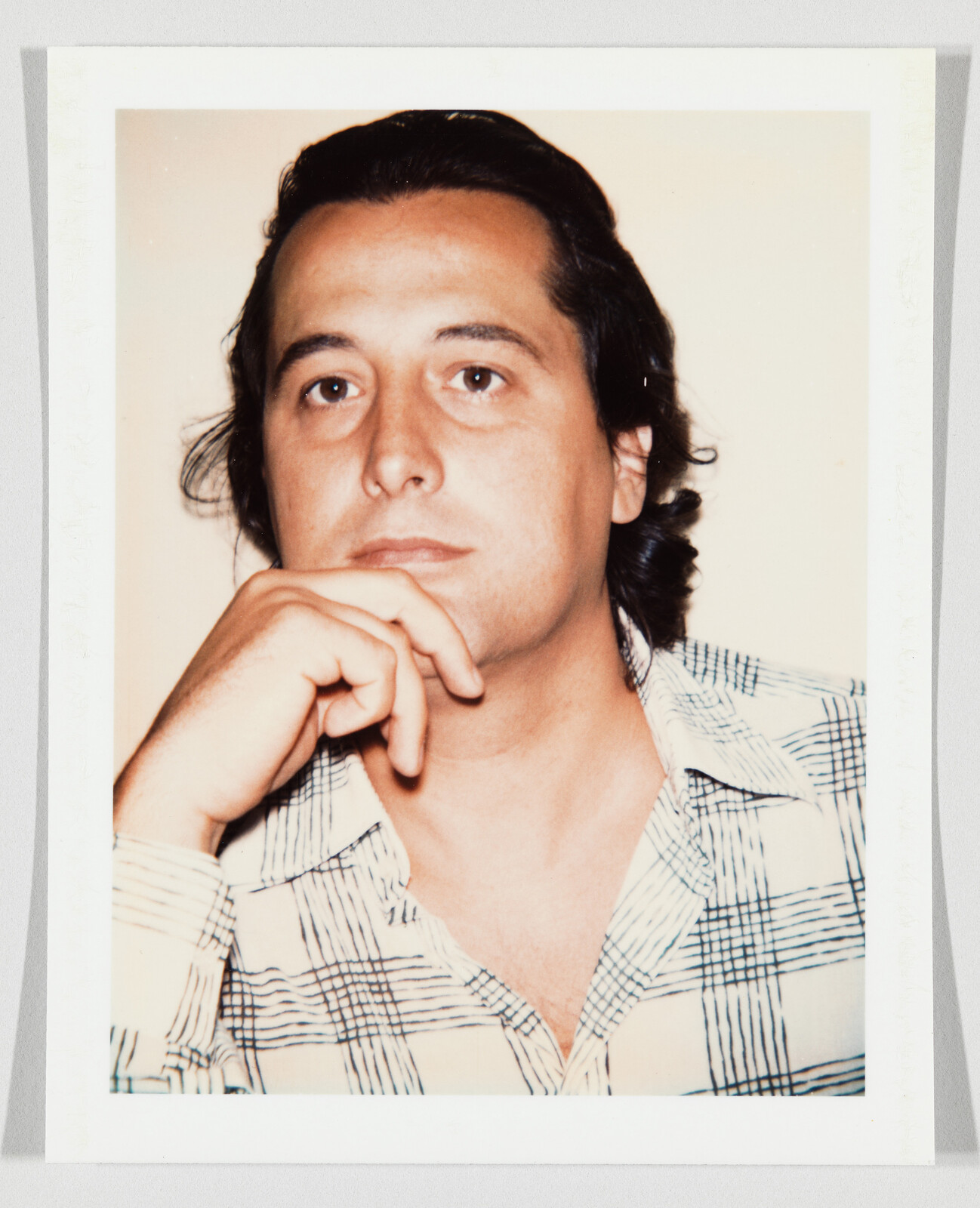 A man in a plaid shirt rests his chin on his hand and looks thoughtful.