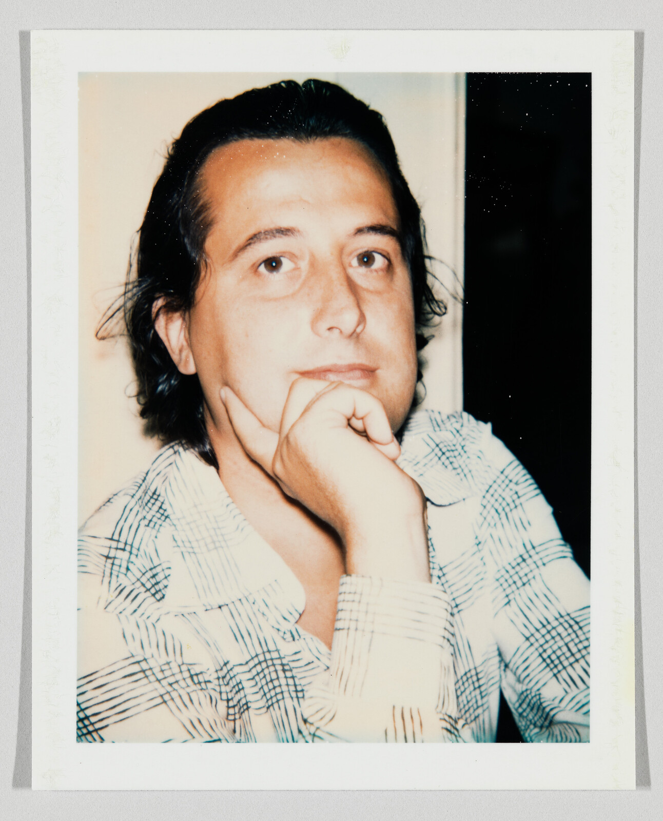 A man with dark hair rests his chin on his hand and looks thoughtfully at the camera.