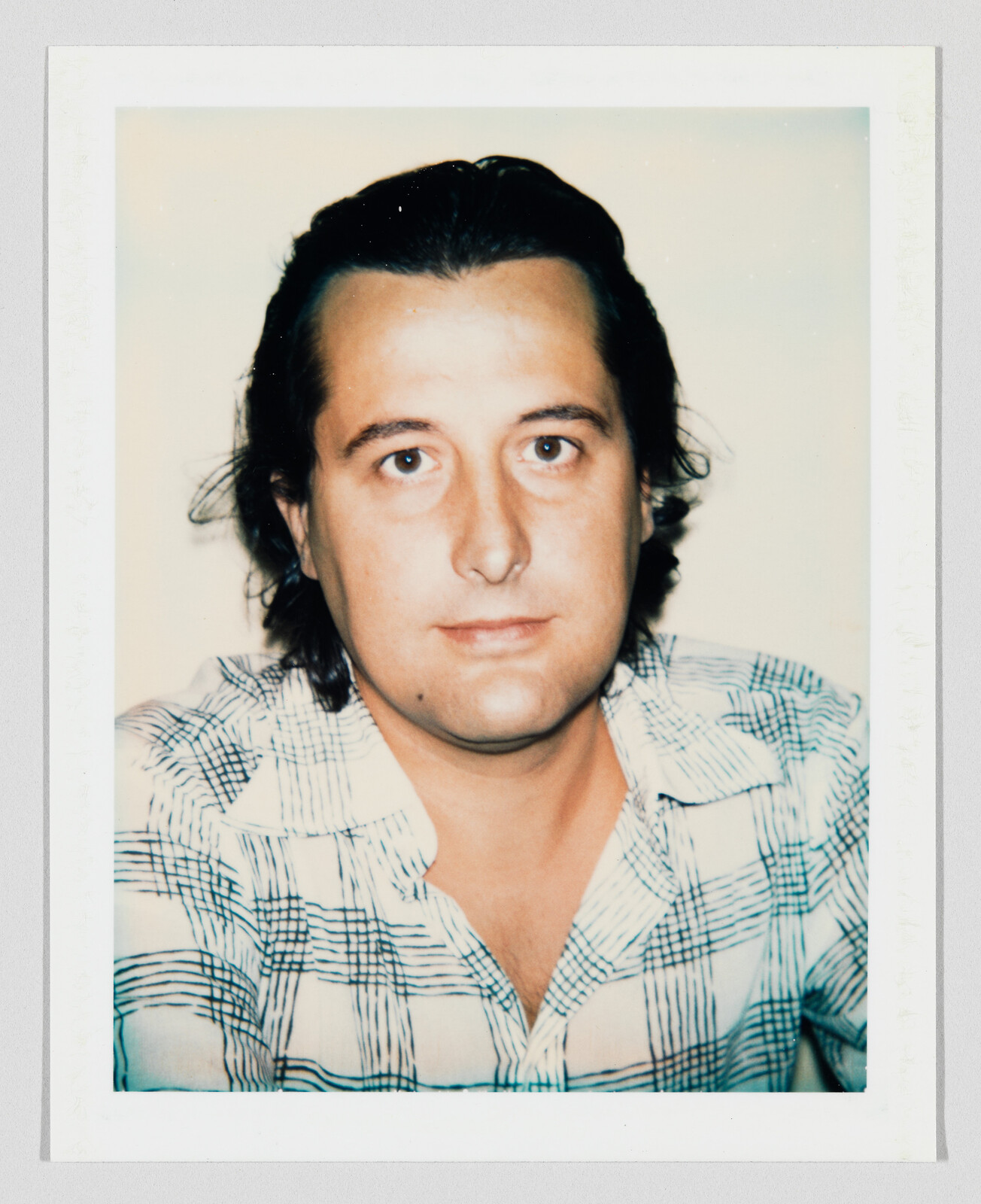 A man with medium-length dark hair looks directly at the camera wearing a patterned button-up shirt.