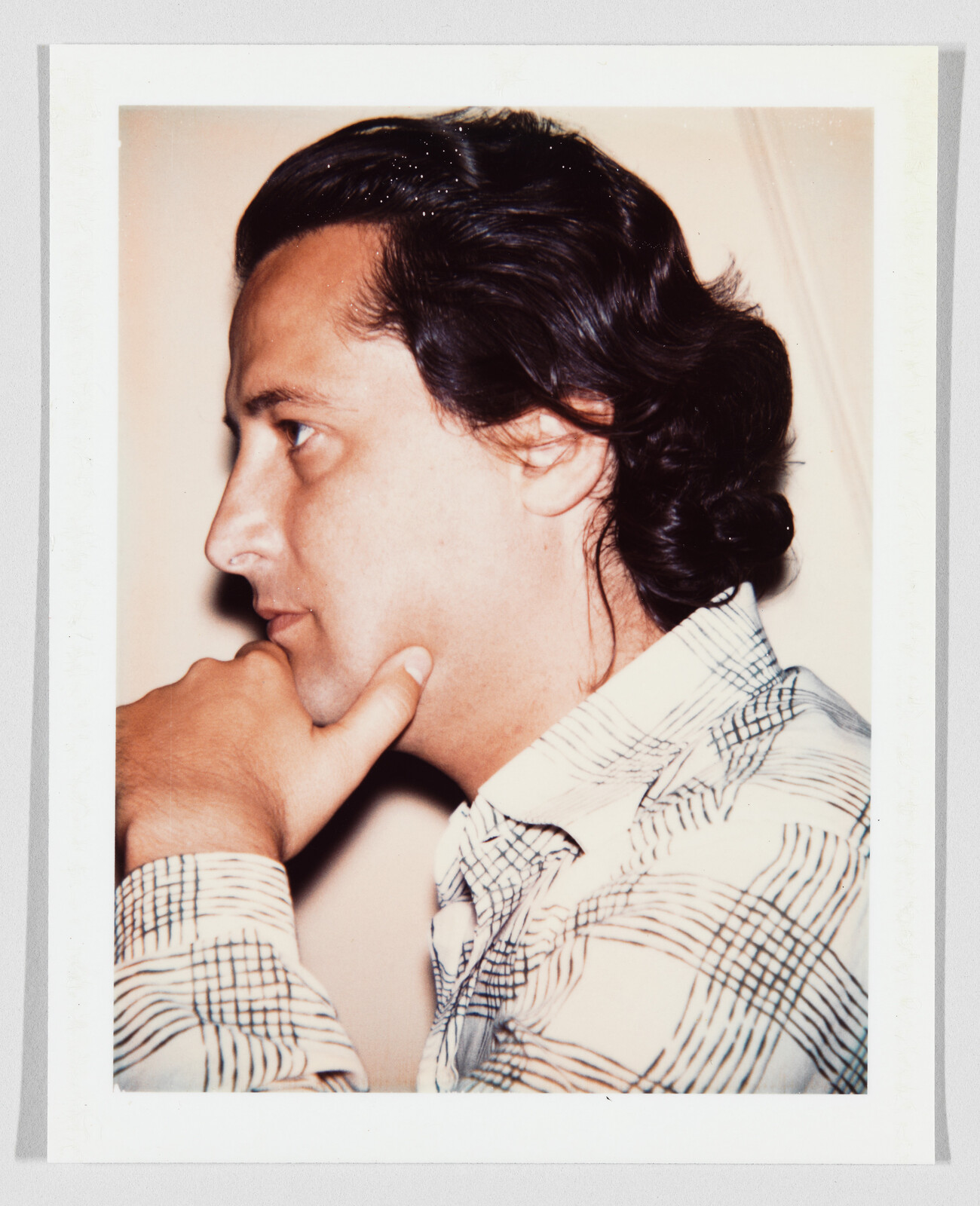 Man in profile resting his chin on his hand and looking thoughtful while wearing a checked shirt.