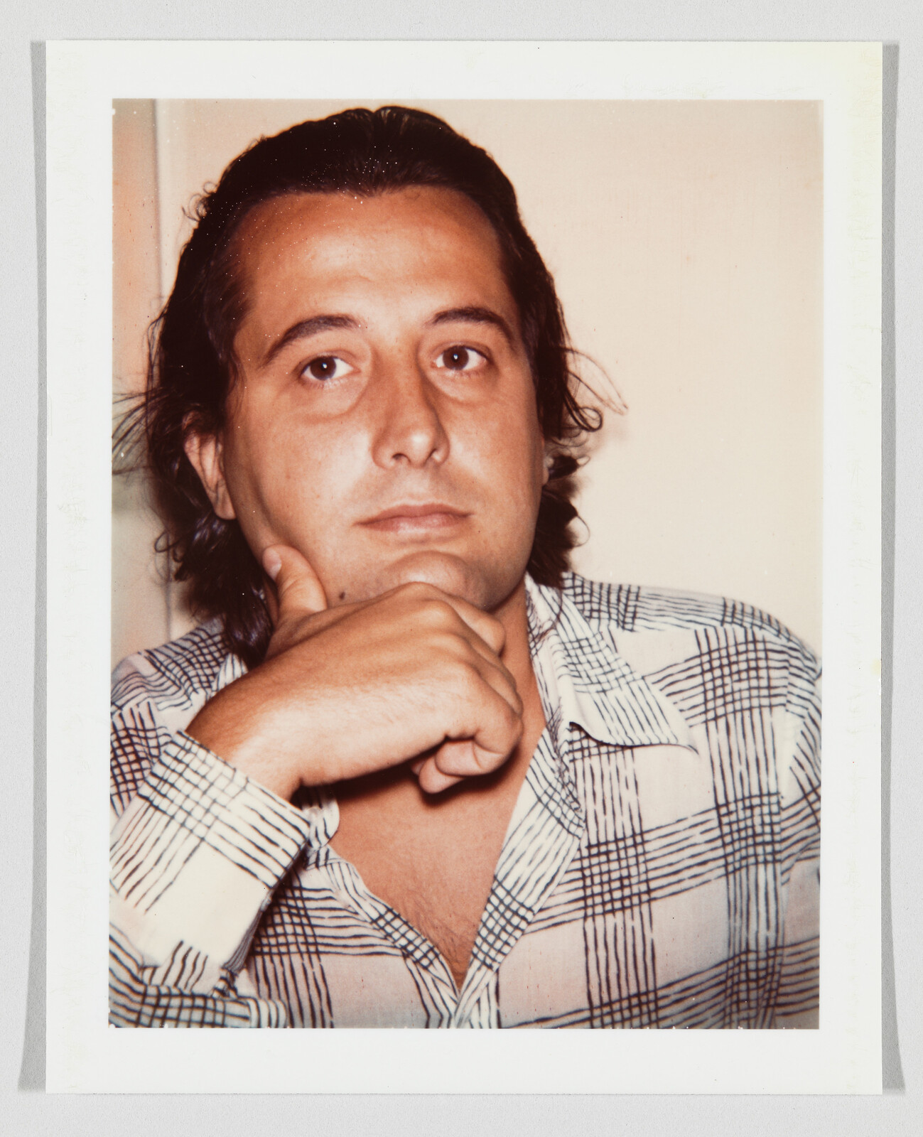 A man rests his chin on his hand while looking thoughtfully toward the camera.