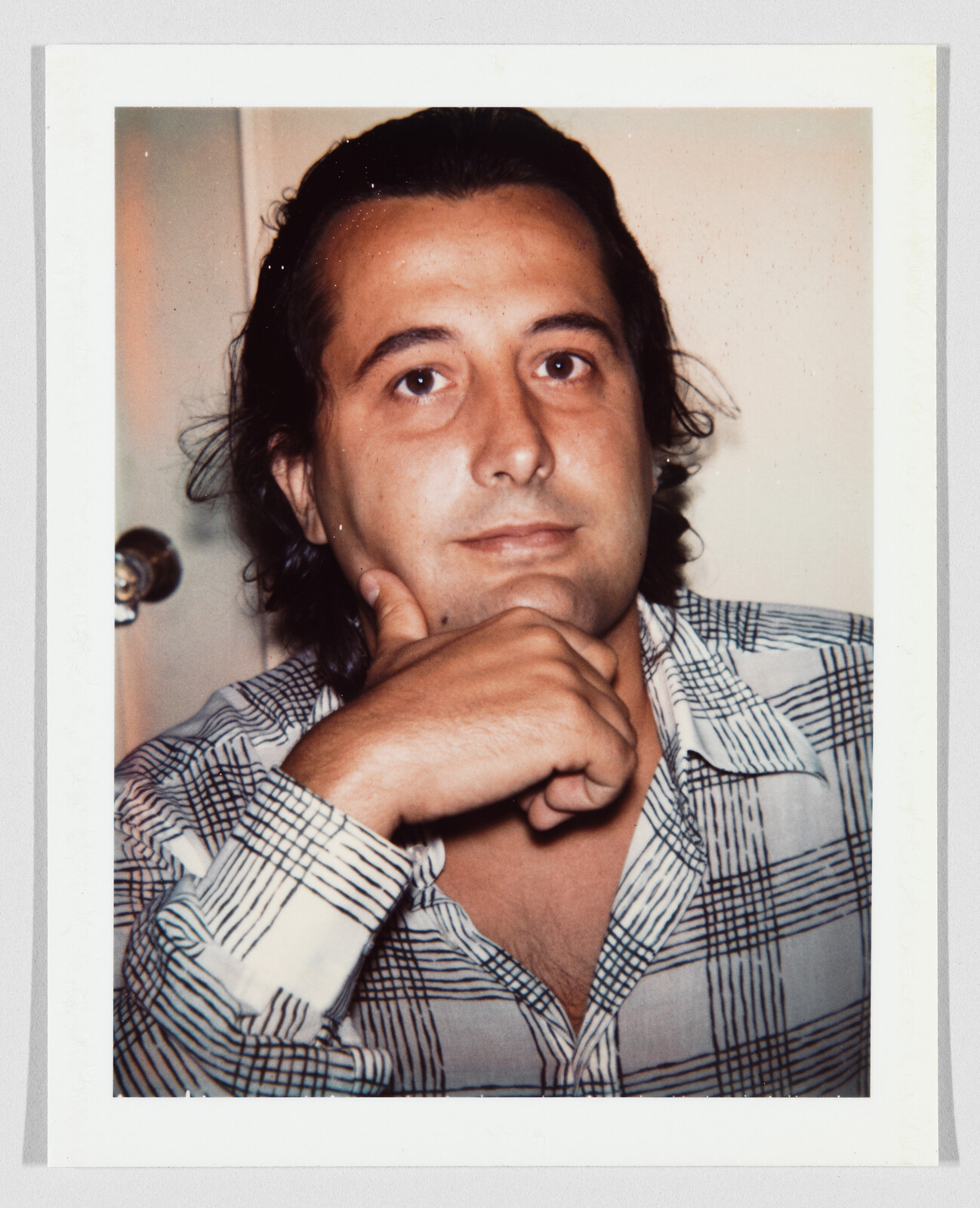 A man with long hair rests his chin on his hand while looking at the camera.