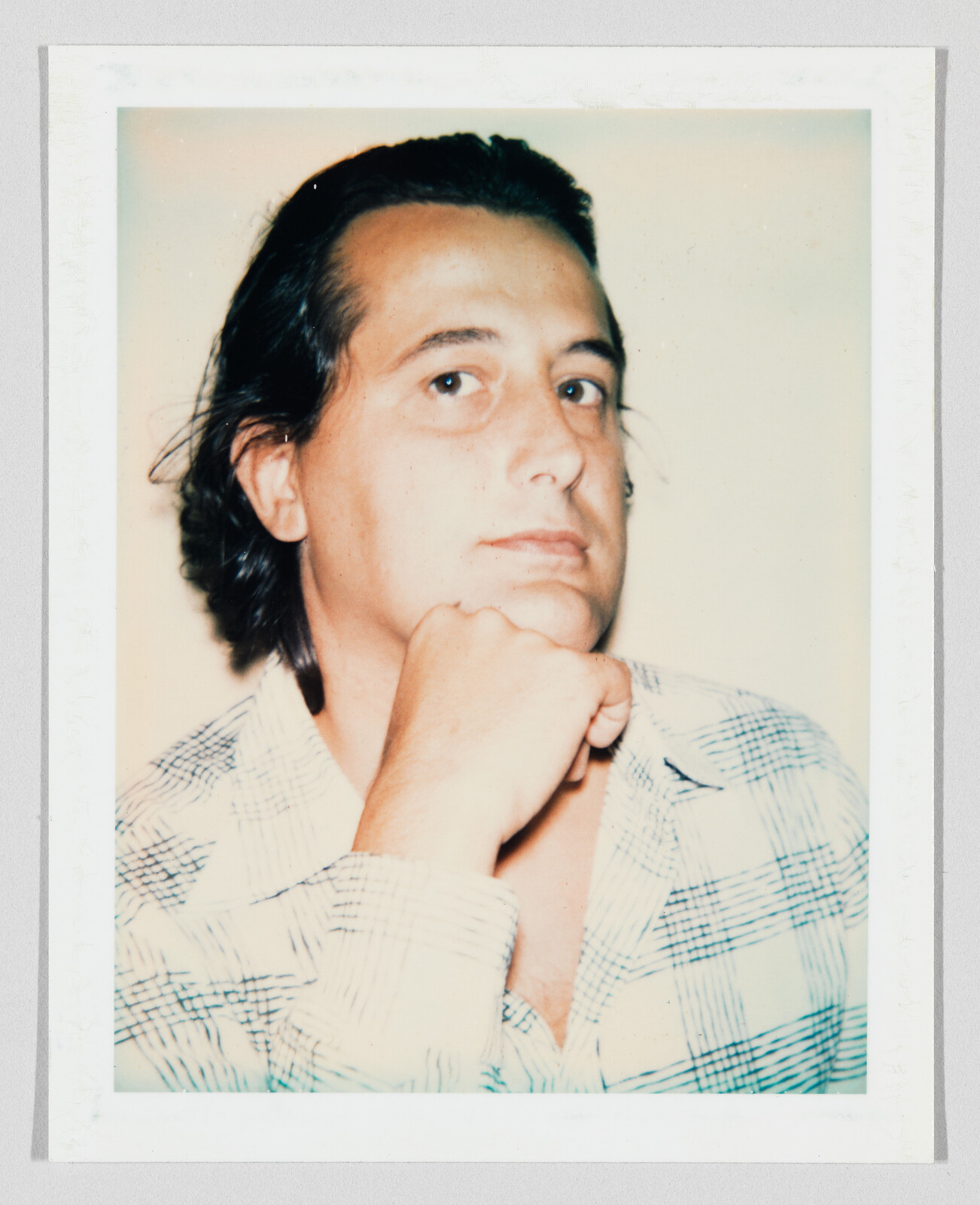 A man with dark hair rests his chin on his hand, looking slightly upward.