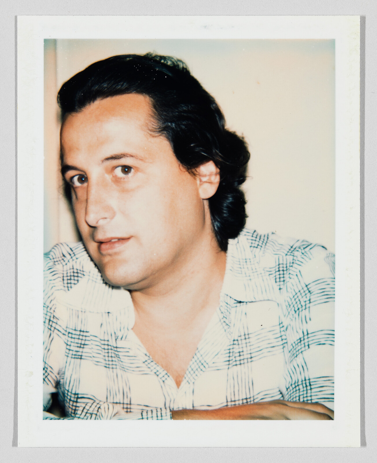 A man with dark hair looks slightly to the side while wearing a checkered shirt.