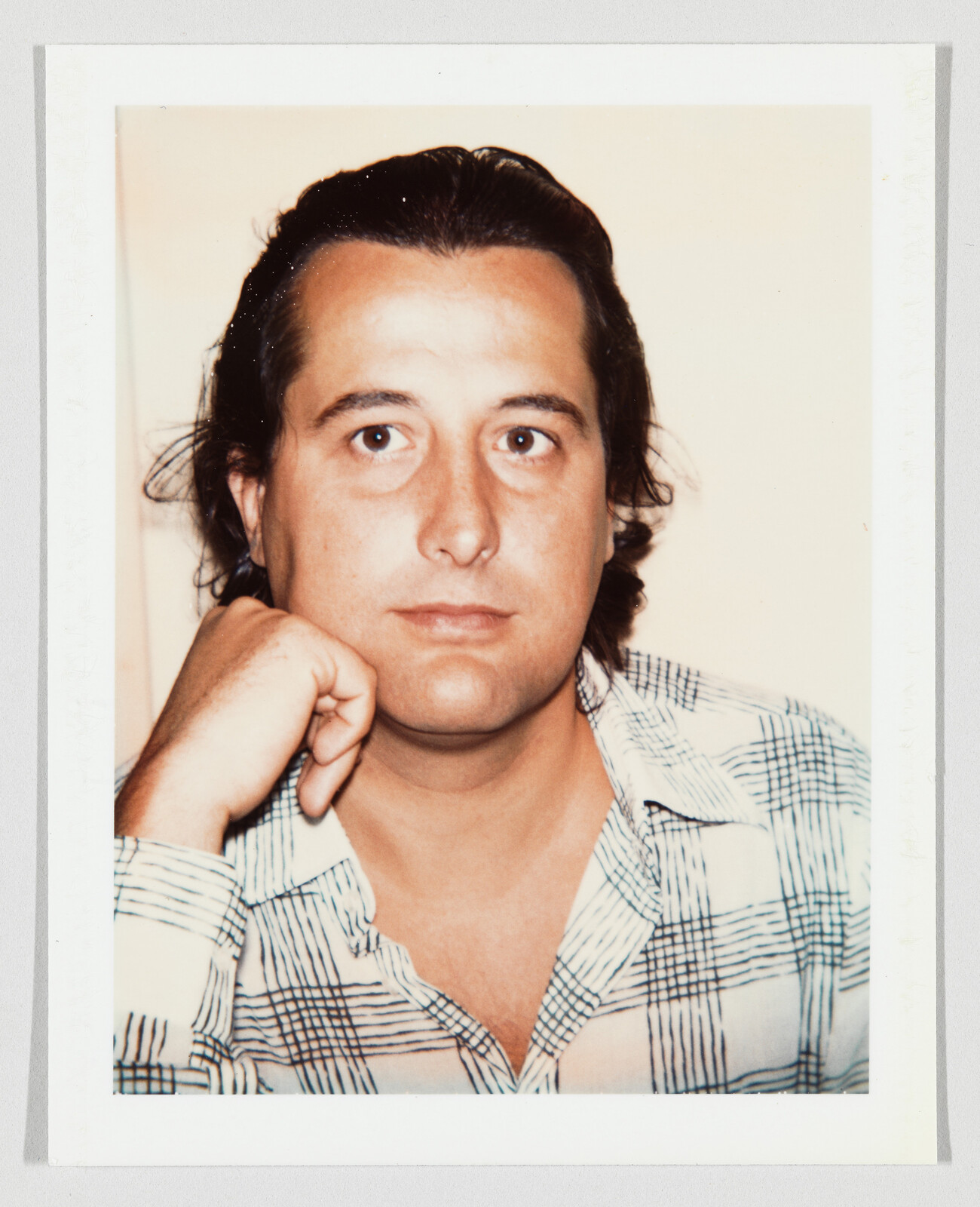 Man with dark hair rests his chin on his hand while looking straight at the camera.